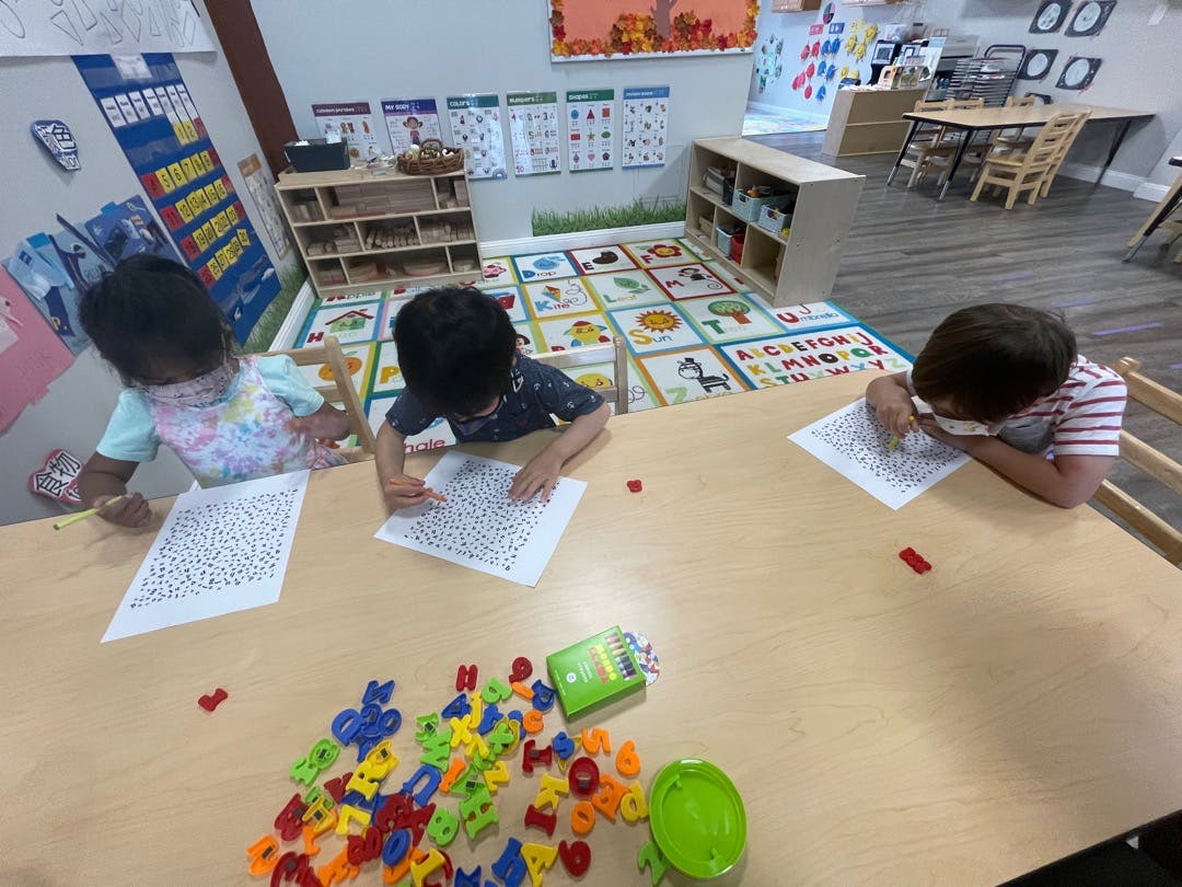 Three children sitting at a table and writing on papers in a classroom