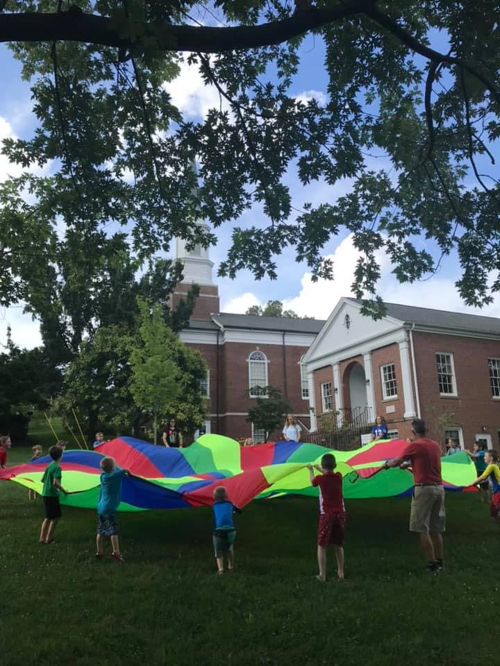 People and children playing with a colorful parachute on a grassy lawn