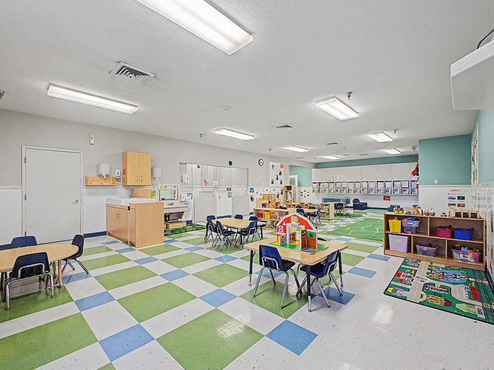 Empty classroom with small tables and chairs, play areas