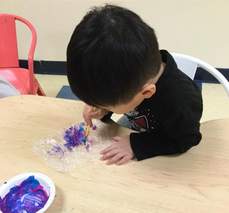 Child painting on bubble wrap at a table