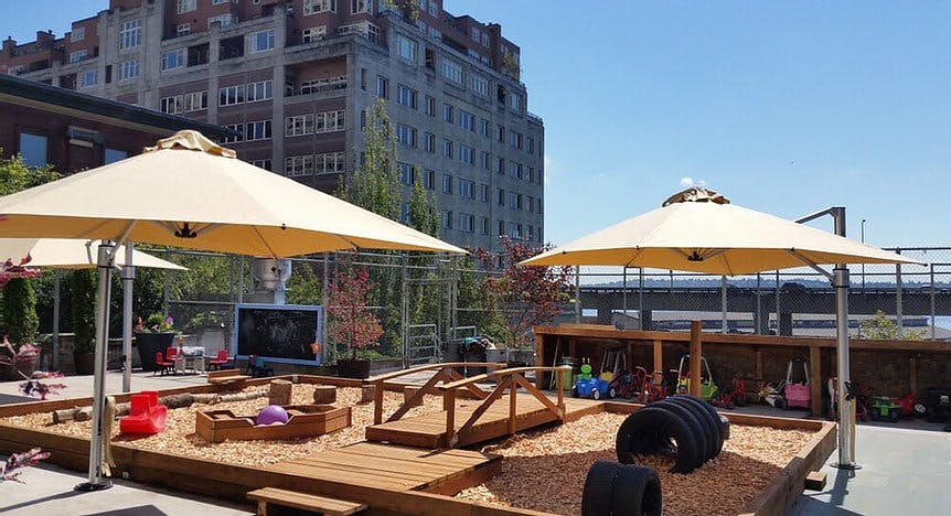 Rooftop playground with wooden structures, wood chips, and large umbrellas