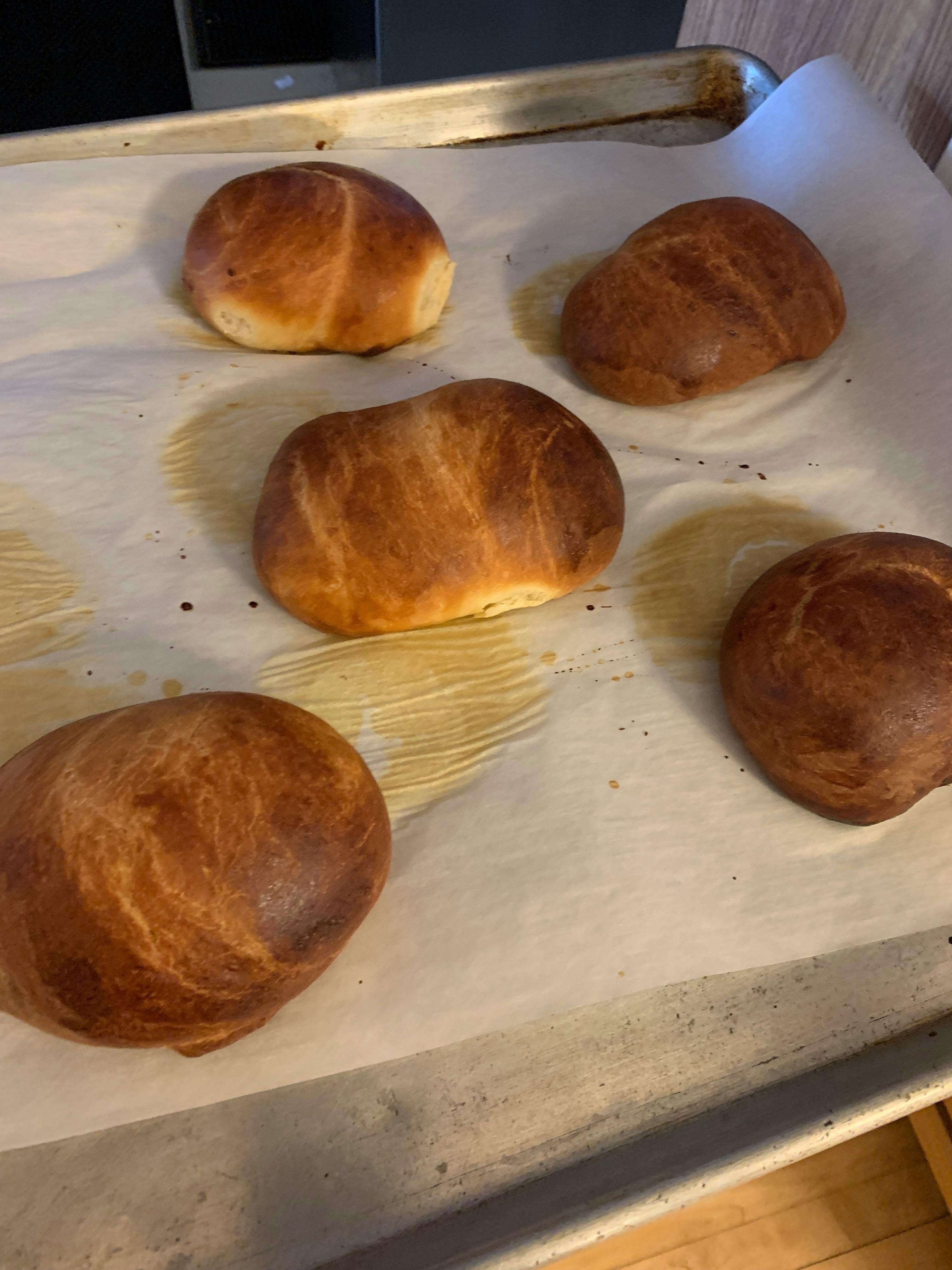 Five baked bread rolls on a baking sheet with parchment paper