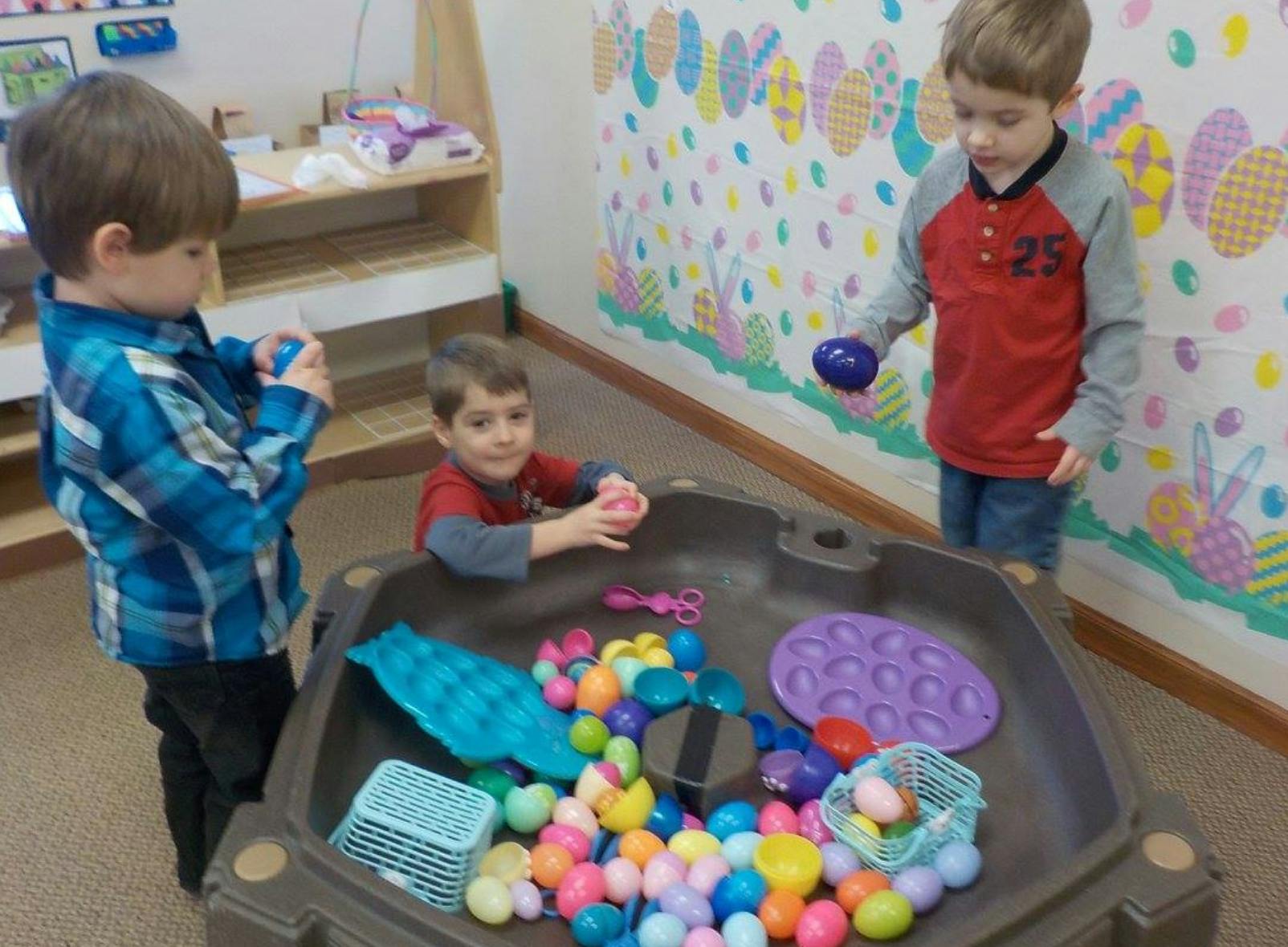 Three children playing with colorful plastic eggs in a sensory bin