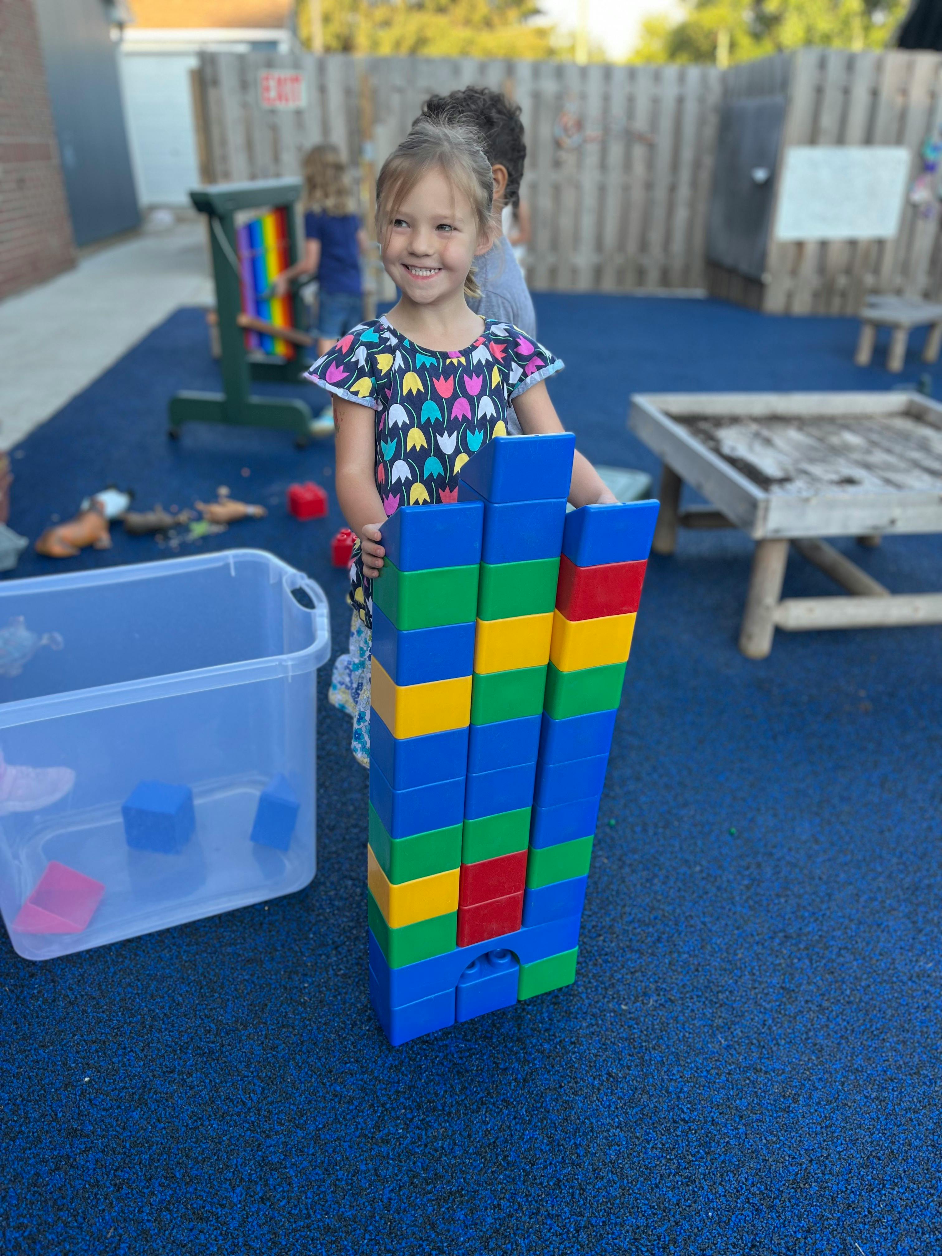 Child standing next to a tall stack of colorful building blocks