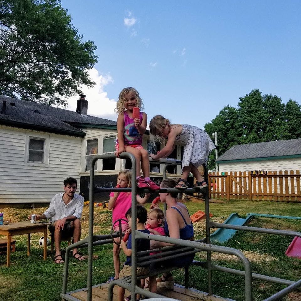 Children and adults on a metal play structure in a yard