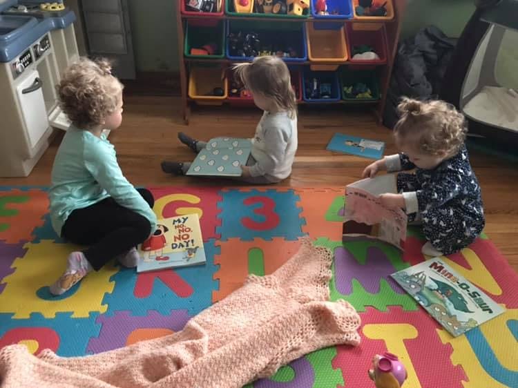 Three children sitting on a colorful mat, looking at books