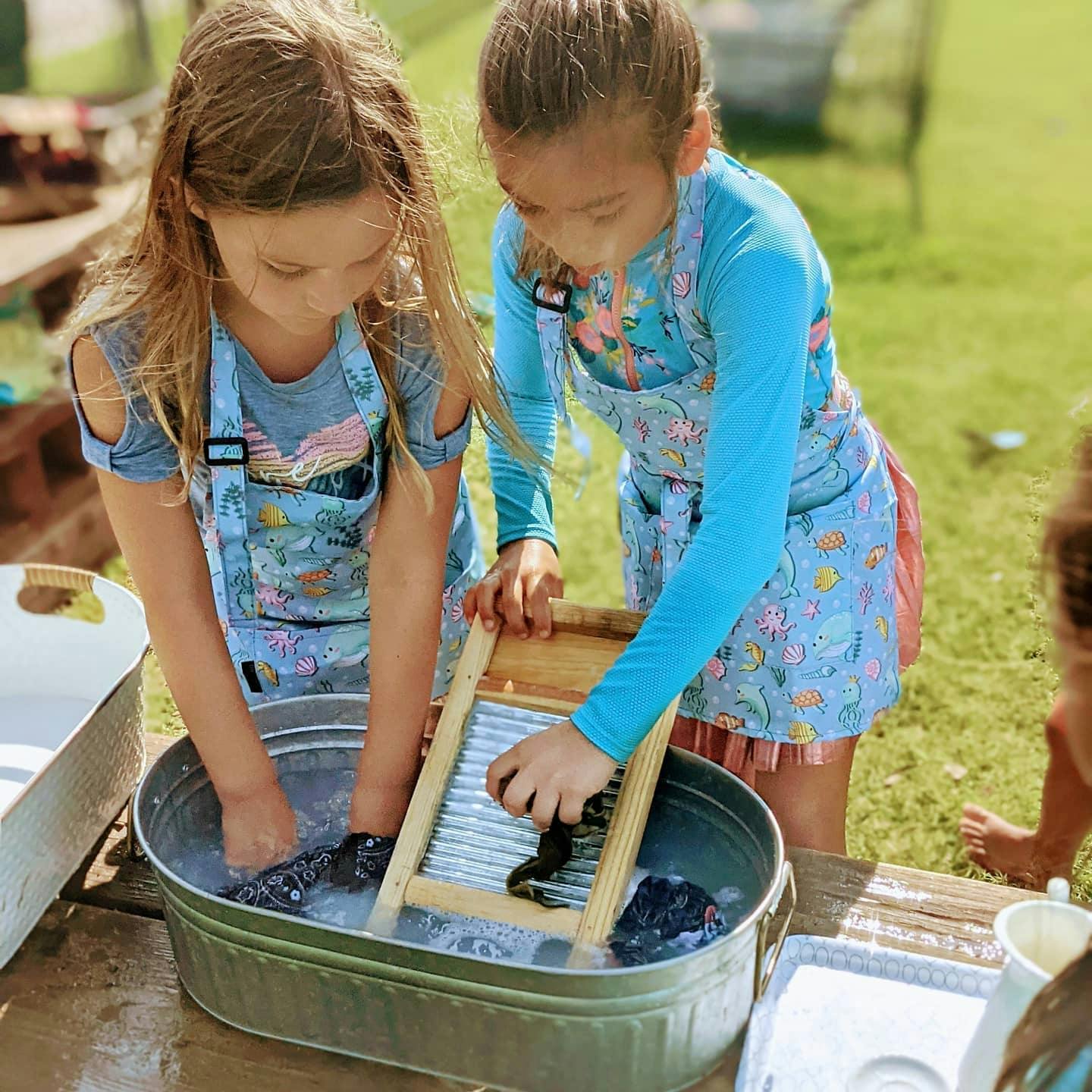 Two children washing items in a tub with a washboard