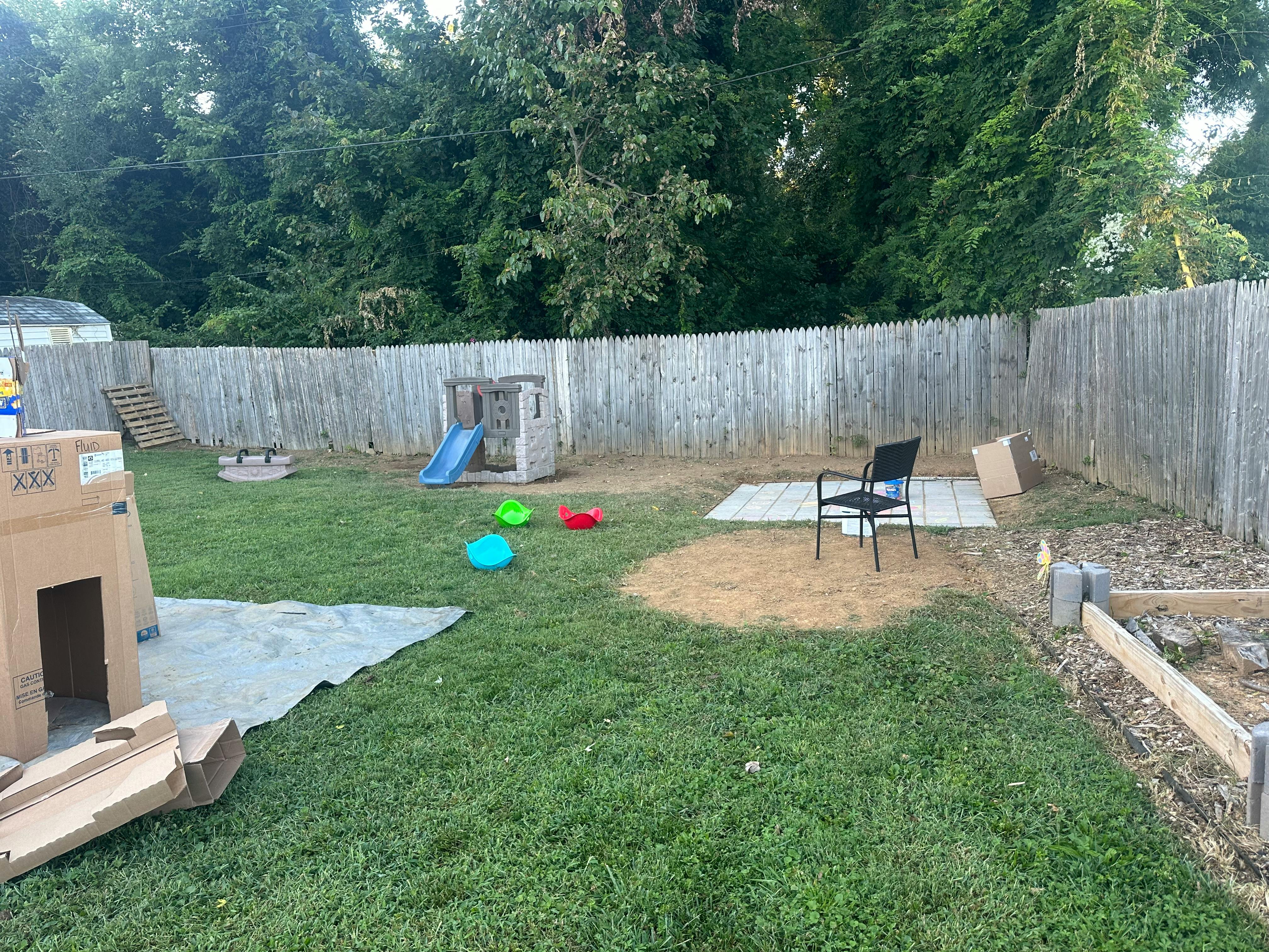 Backyard with a wooden fence, play structure with slide, and cardboard fort