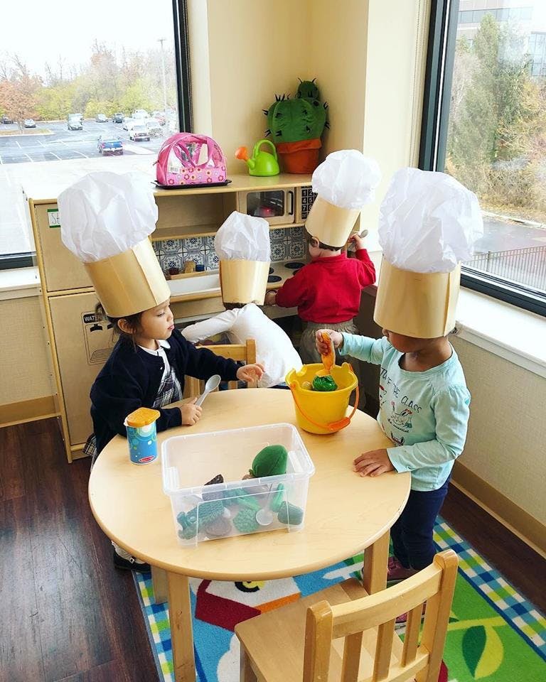Children wearing chef hats playing at a table in a classroom