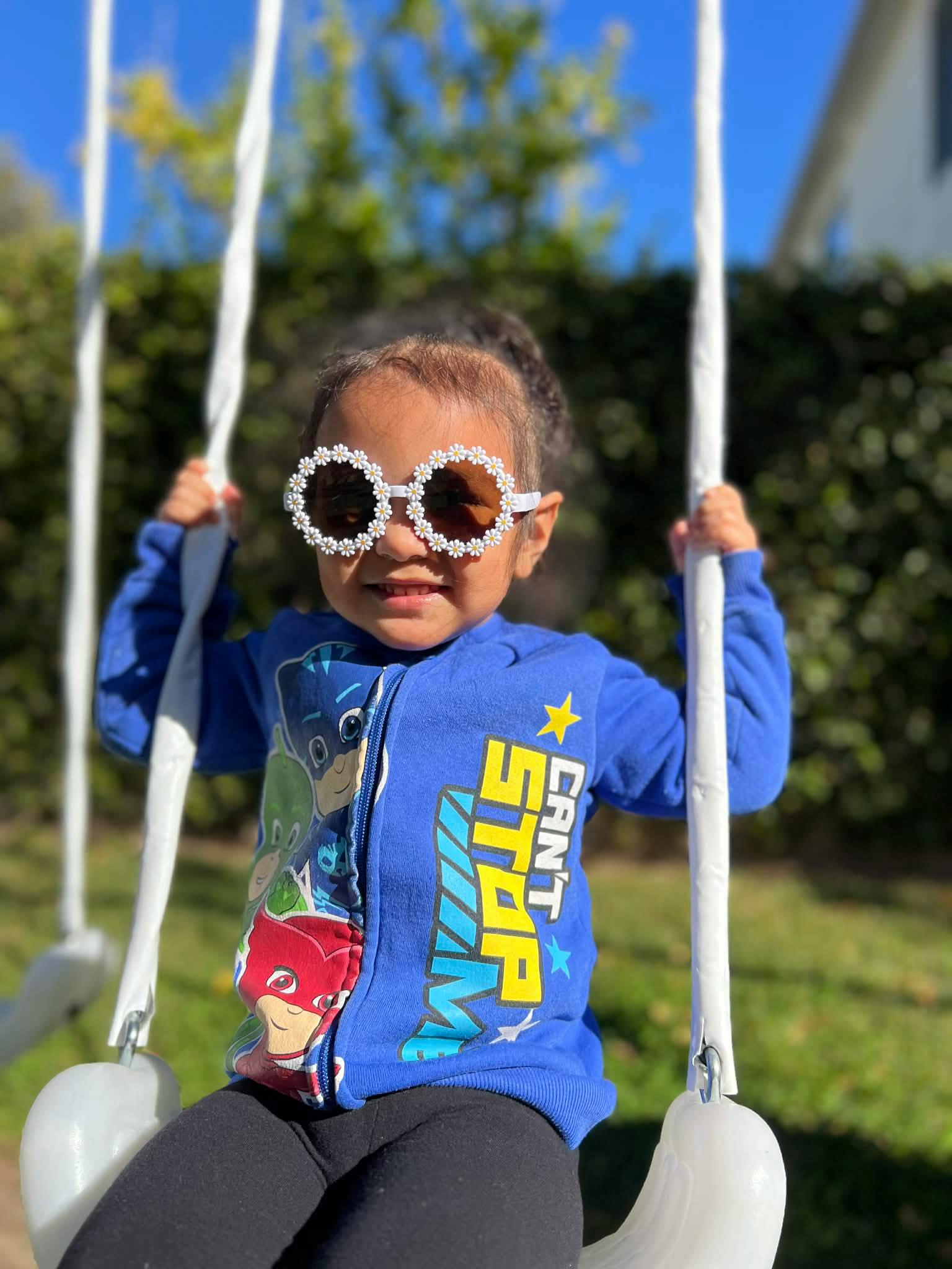 Child wearing flower-shaped sunglasses sitting on a swing