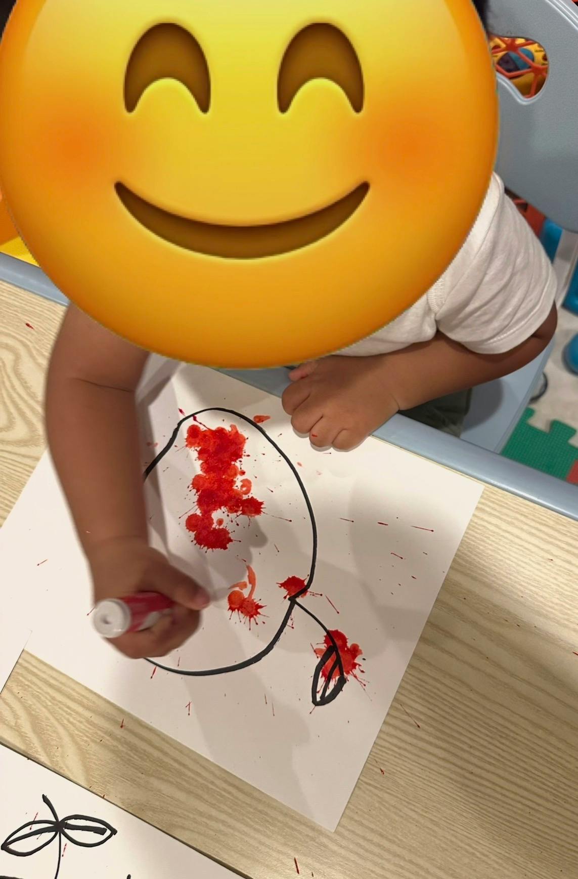 Child splashing red paint onto a drawing of an apple