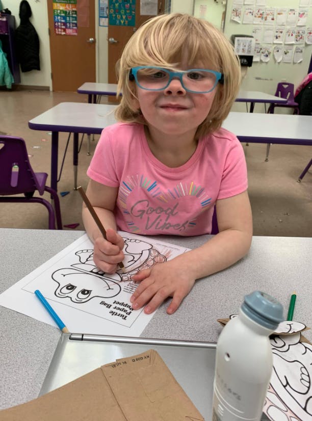 Child coloring a drawing of a frog at a desk in a classroom