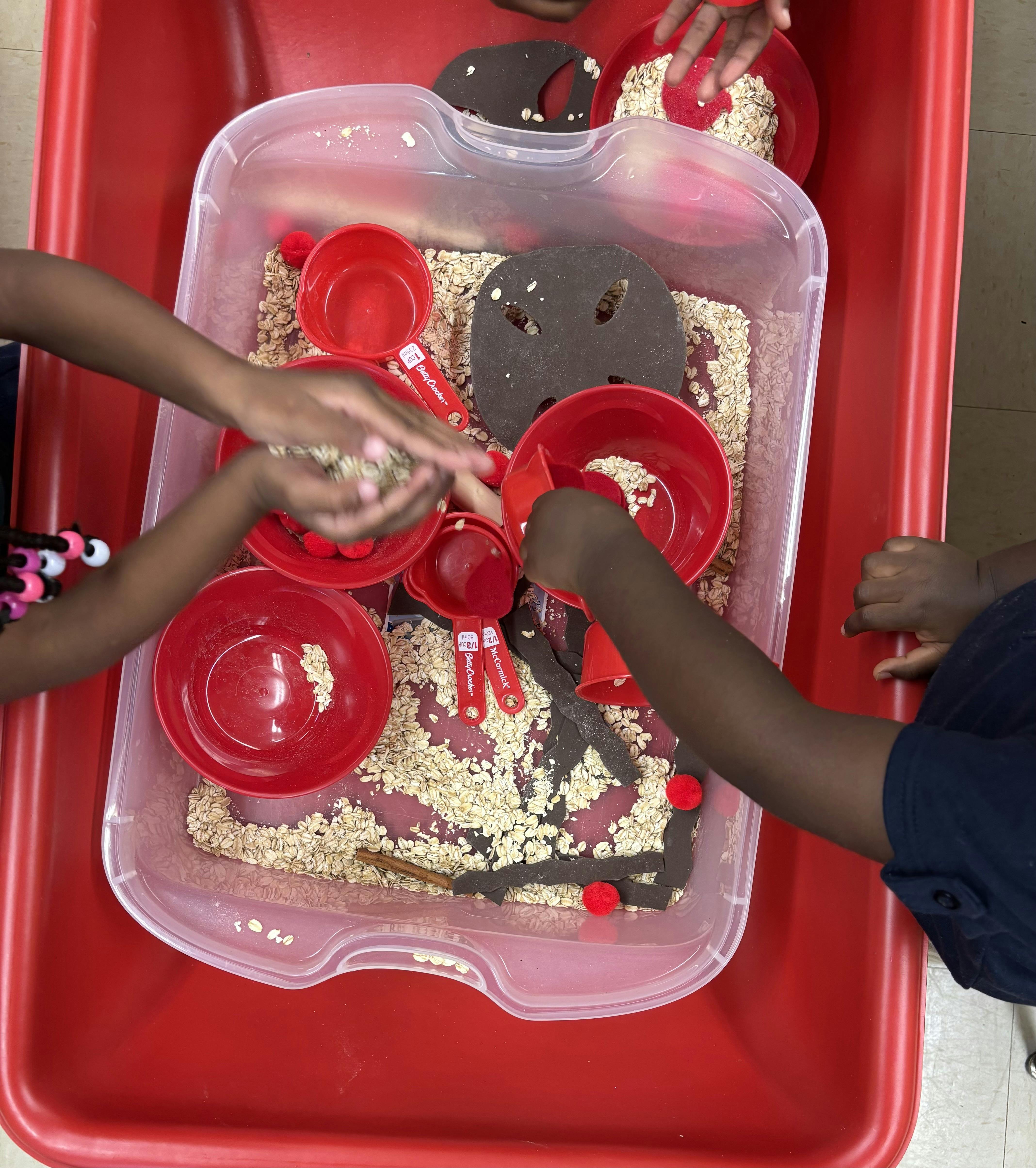 People playing with oats and red bowls in a sensory bin