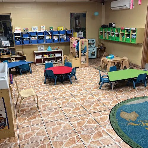 Classroom with small tables and chairs, shelves with bins, and a play kitchen