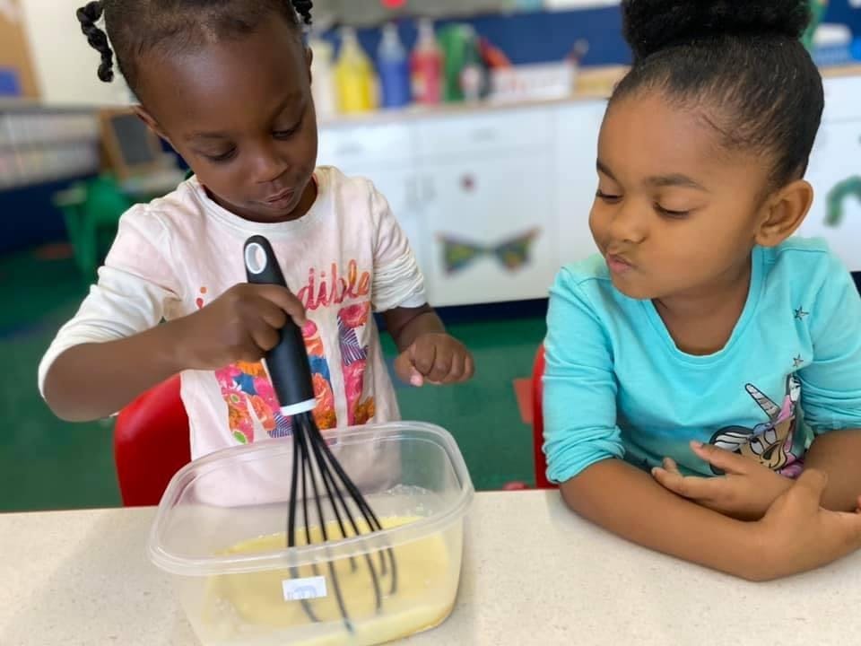 Child whisking liquid in a container, another child watching