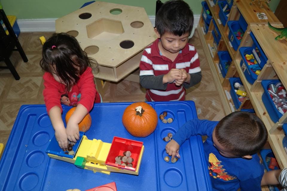 Three children playing with pumpkins and small objects at a blue table