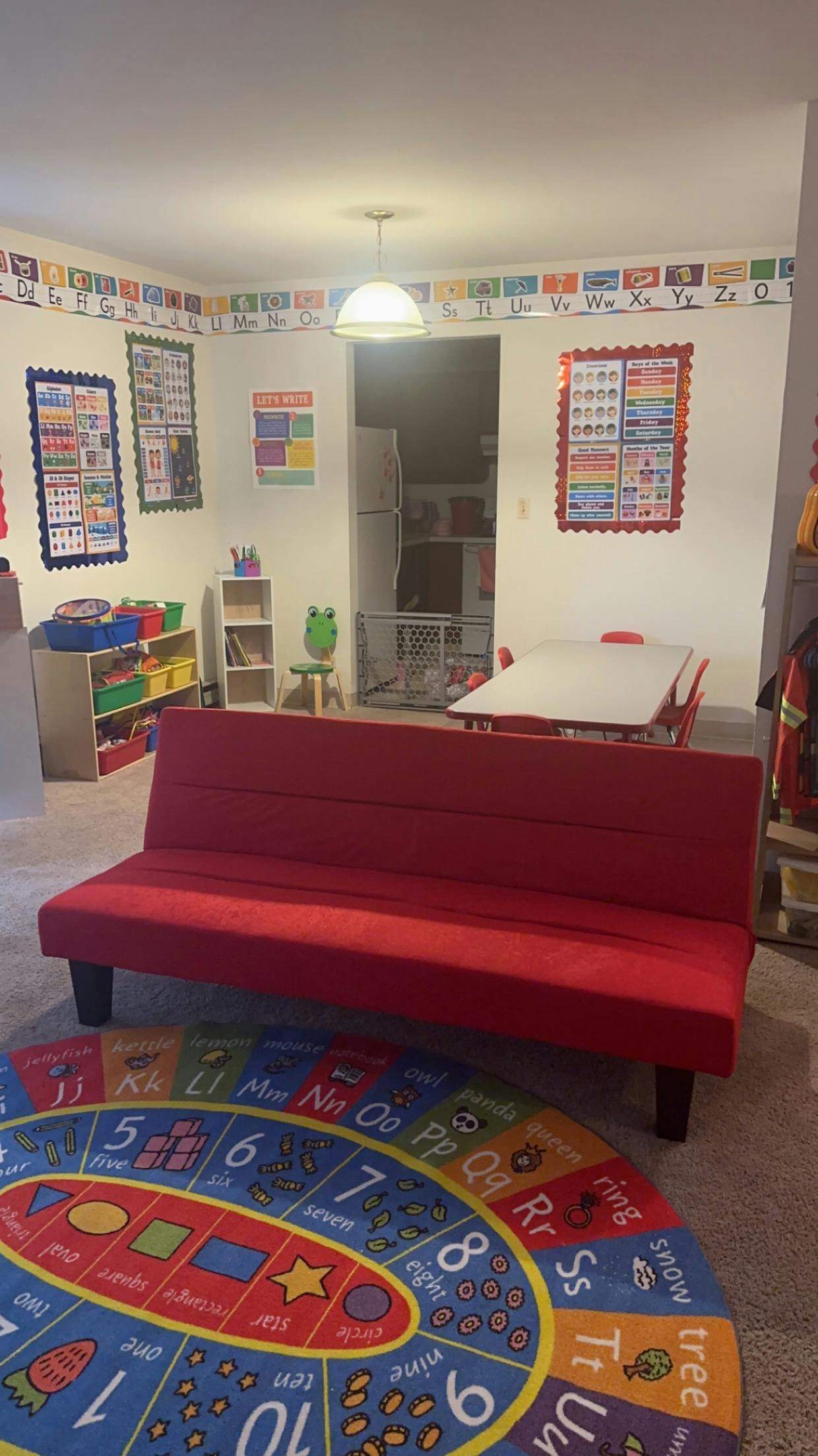 Red couch in a room with an alphabet rug and educational posters