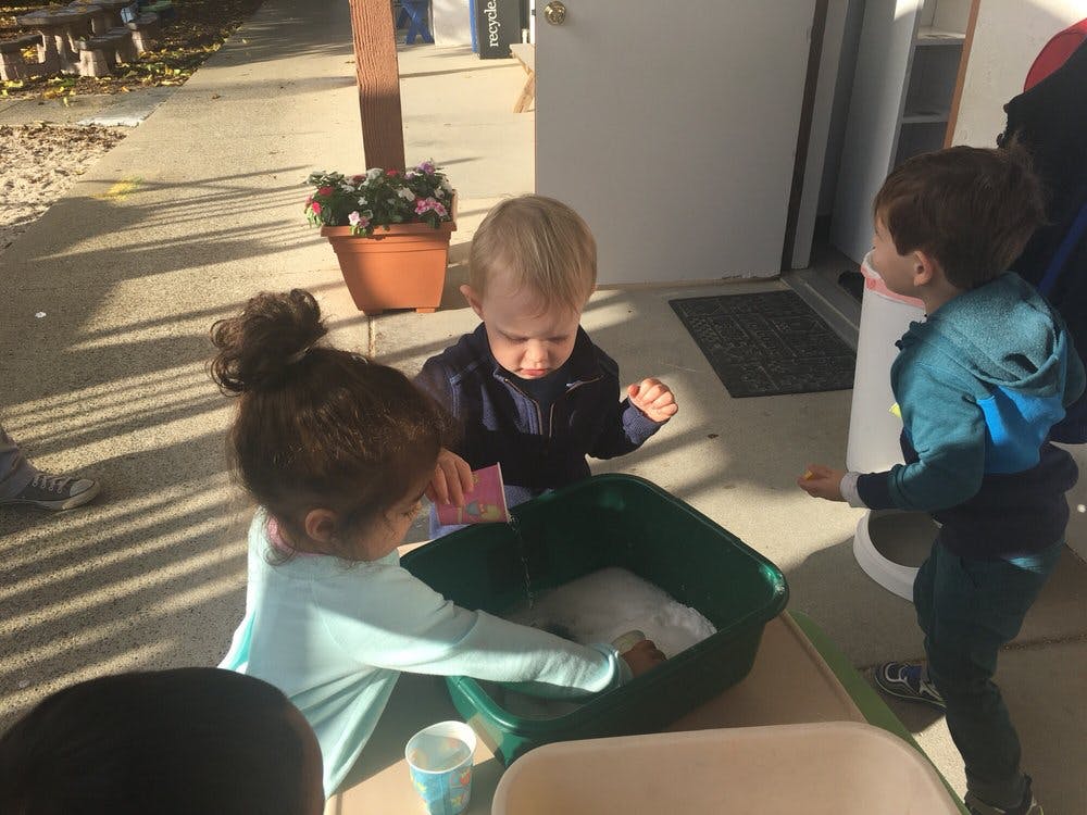 Three children playing with a green tub outdoors