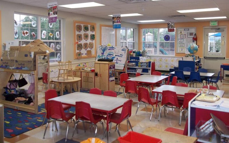 An empty classroom with small tables and chairs, artwork on walls and windows