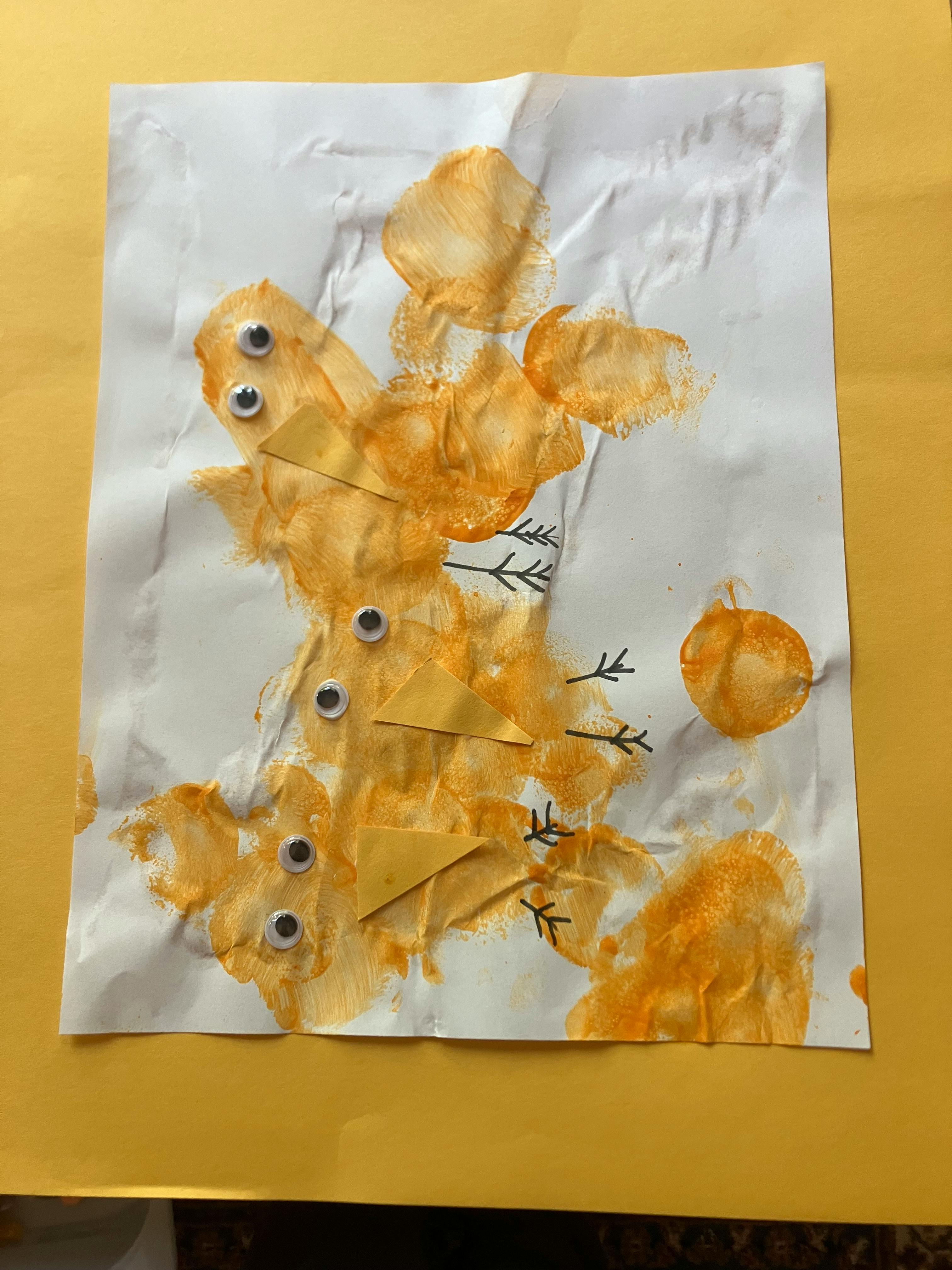 Childs artwork with orange paint dabs, googly eyes, and paper triangles