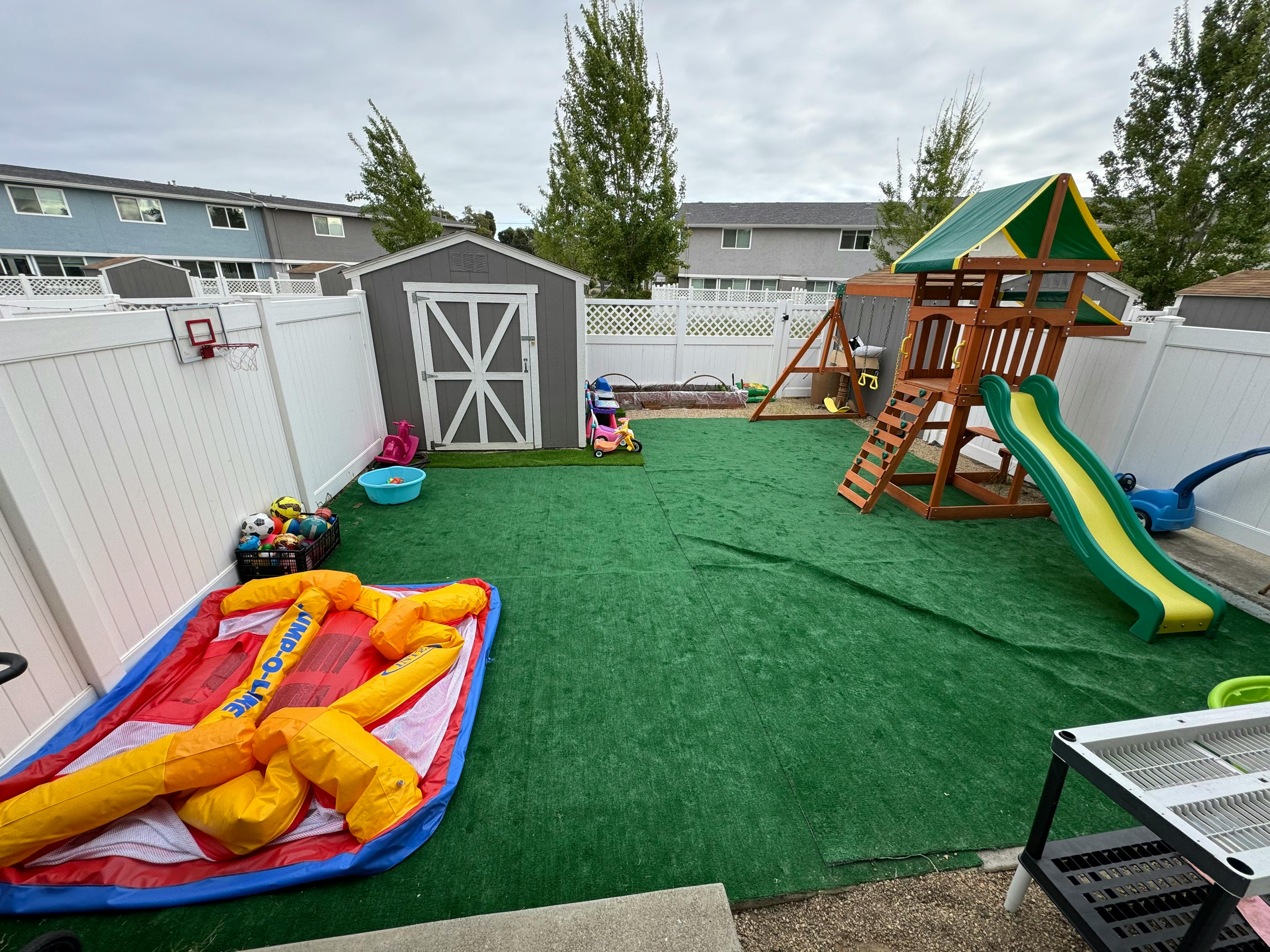 Backyard with artificial turf, a shed, and a playset with a slide