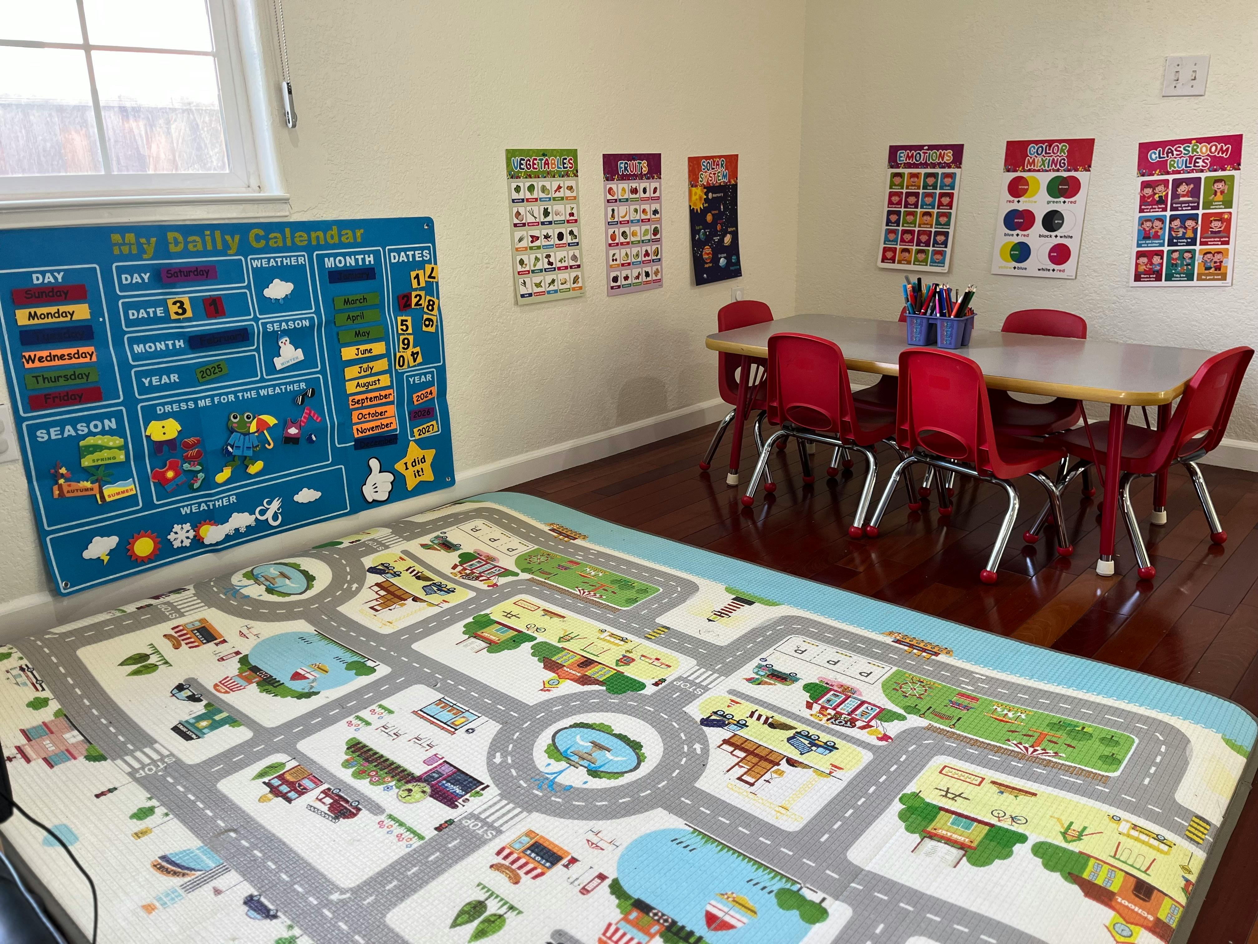 Classroom with a playmat, a daily calendar, and a table with red chairs
