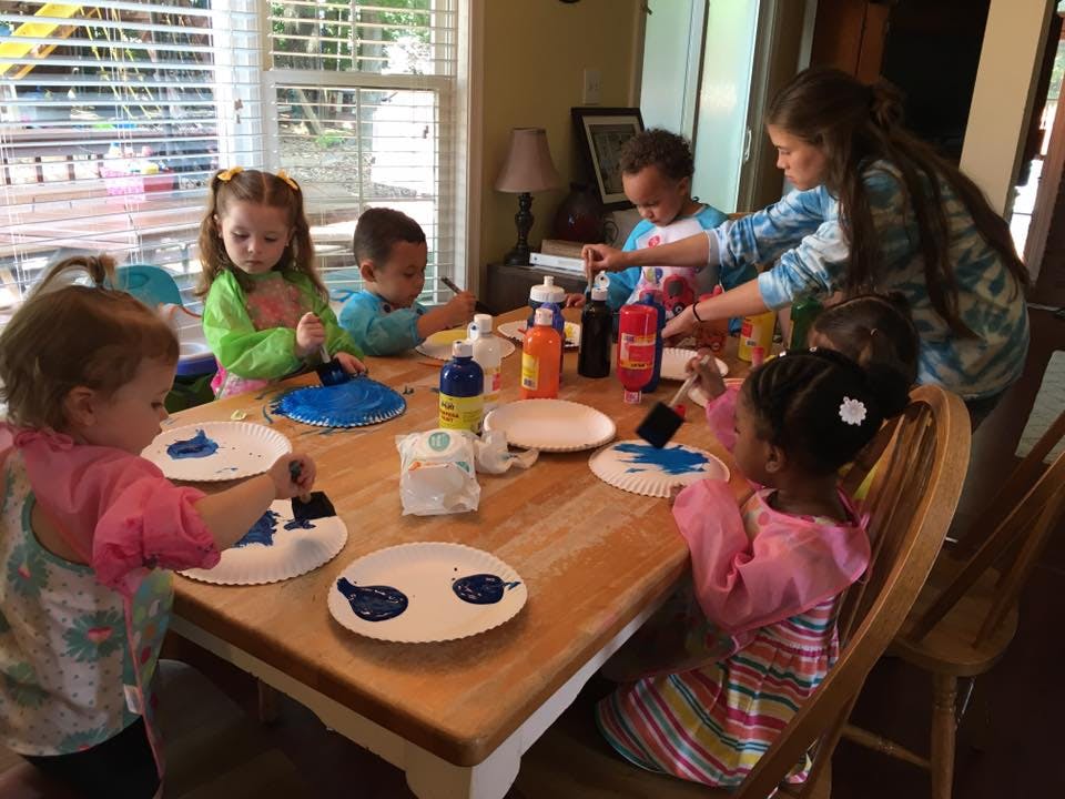 Children and a person painting paper plates at a table
