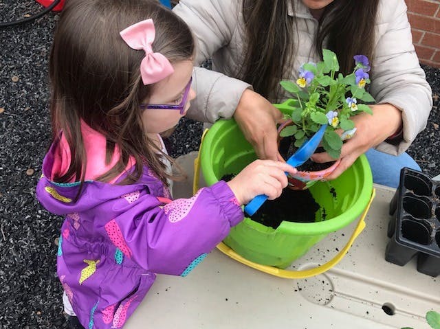 Child and person planting flowers in a green bucket