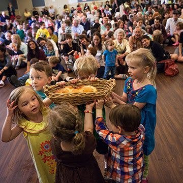 Children holding a basket of bread in front of a crowd of people