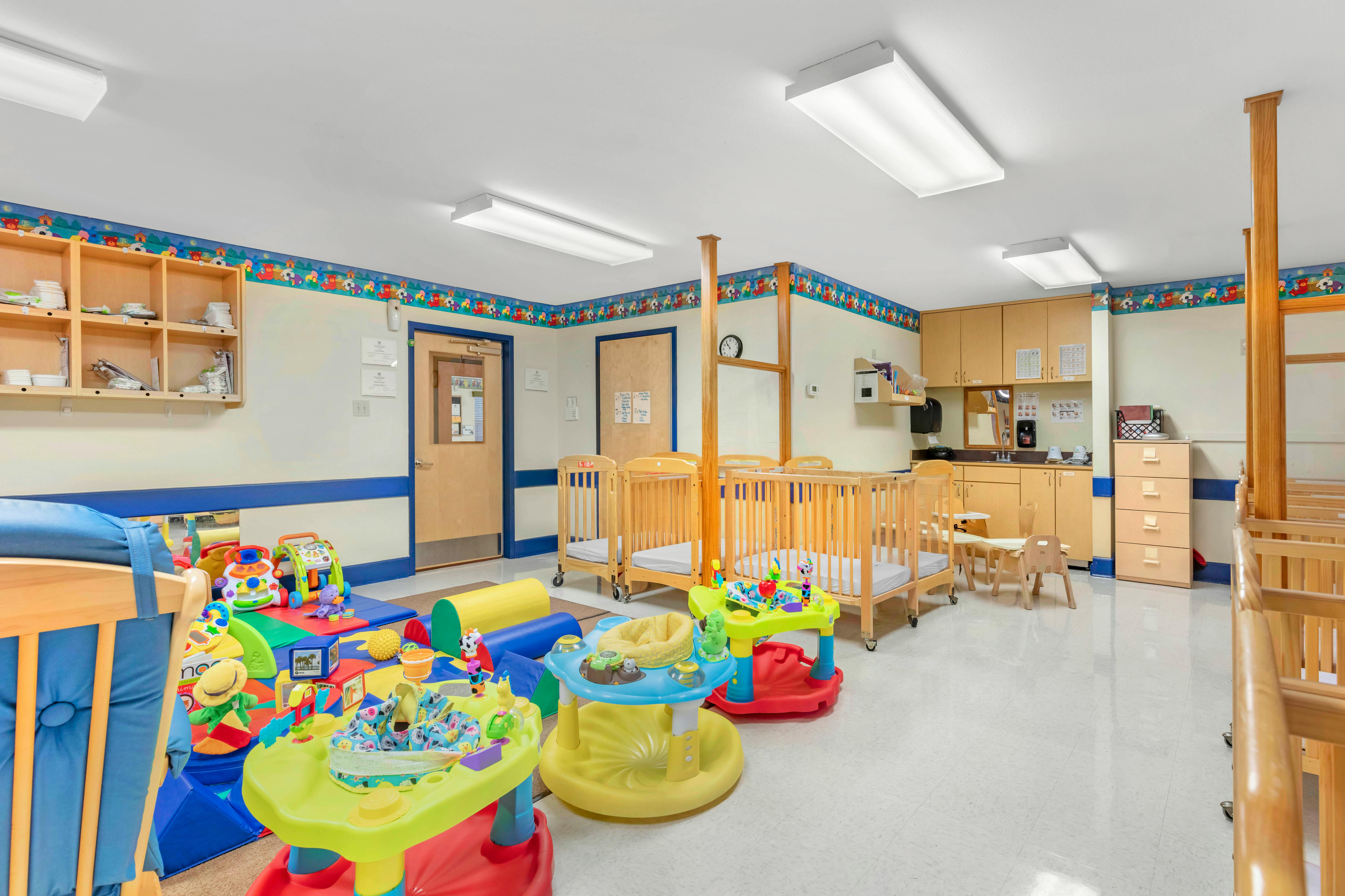 Baby room with wooden cribs, play mats, infant play stations, and wooden cabinets