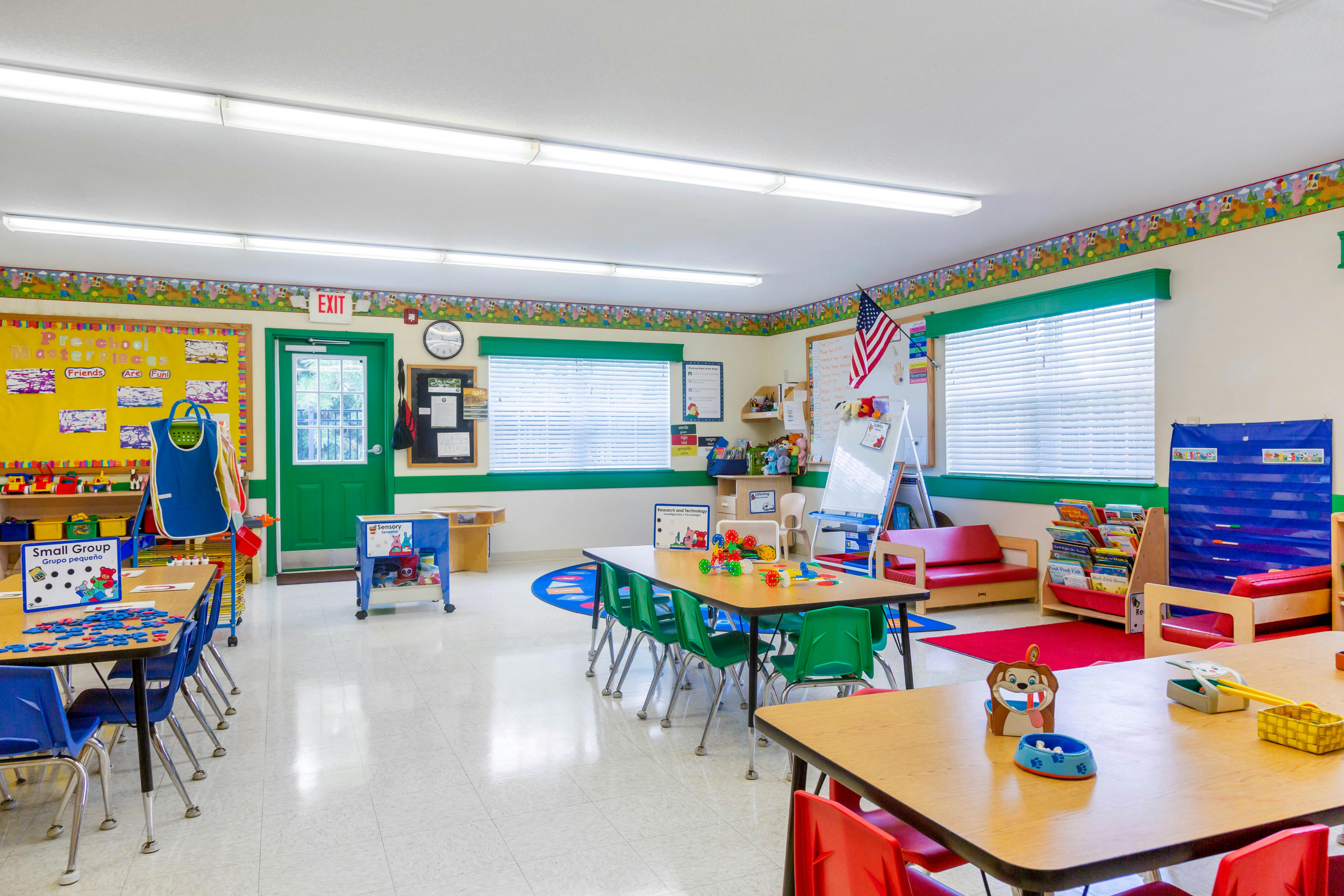 An empty preschool classroom with small tables and chairs, toys, and educational posters