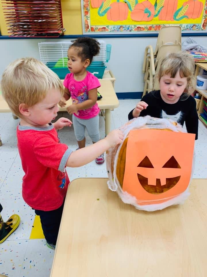 Three children interacting with a pumpkin decoration in a classroom