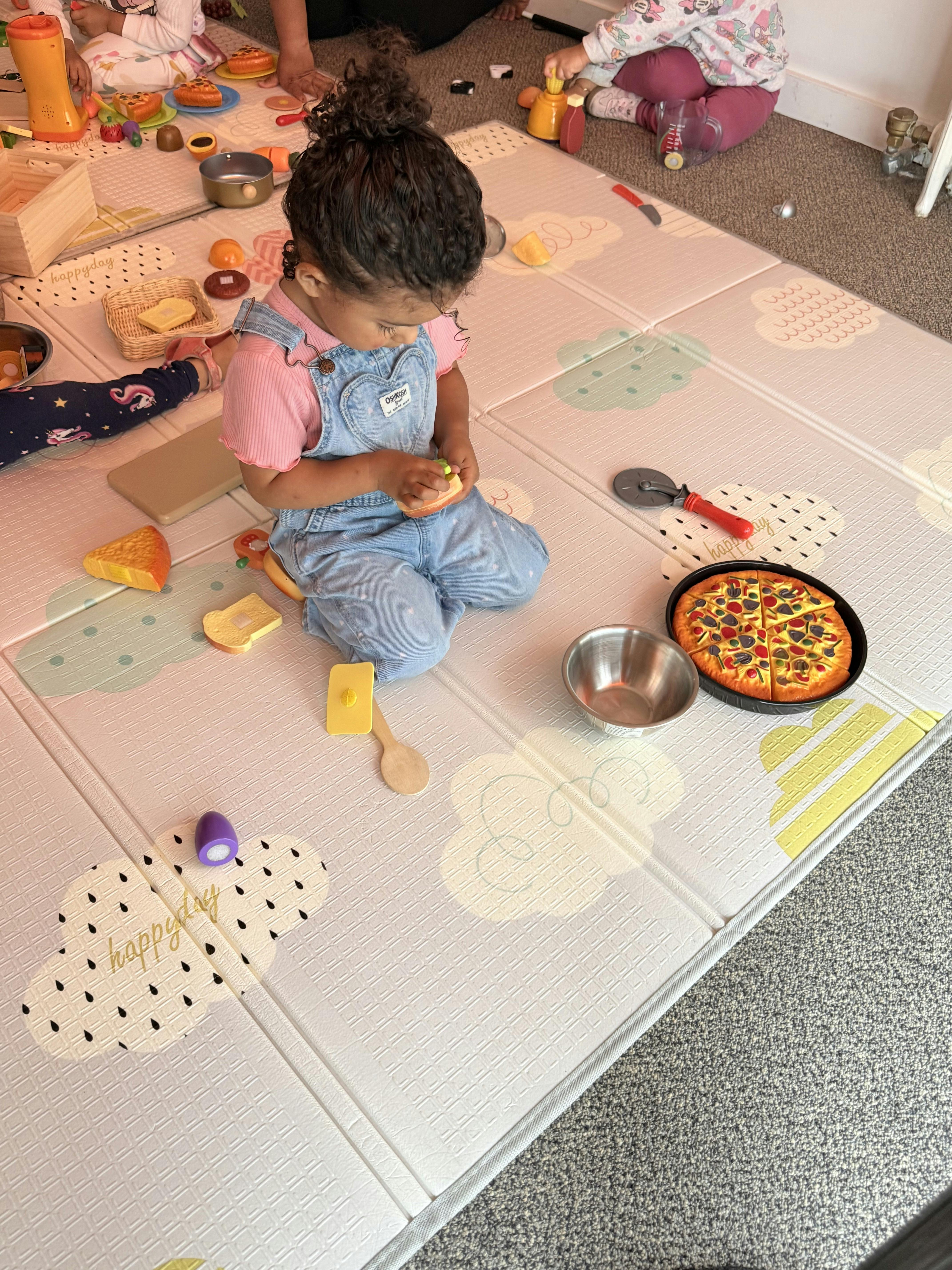Child playing with toy kitchen food and utensils on a floor mat