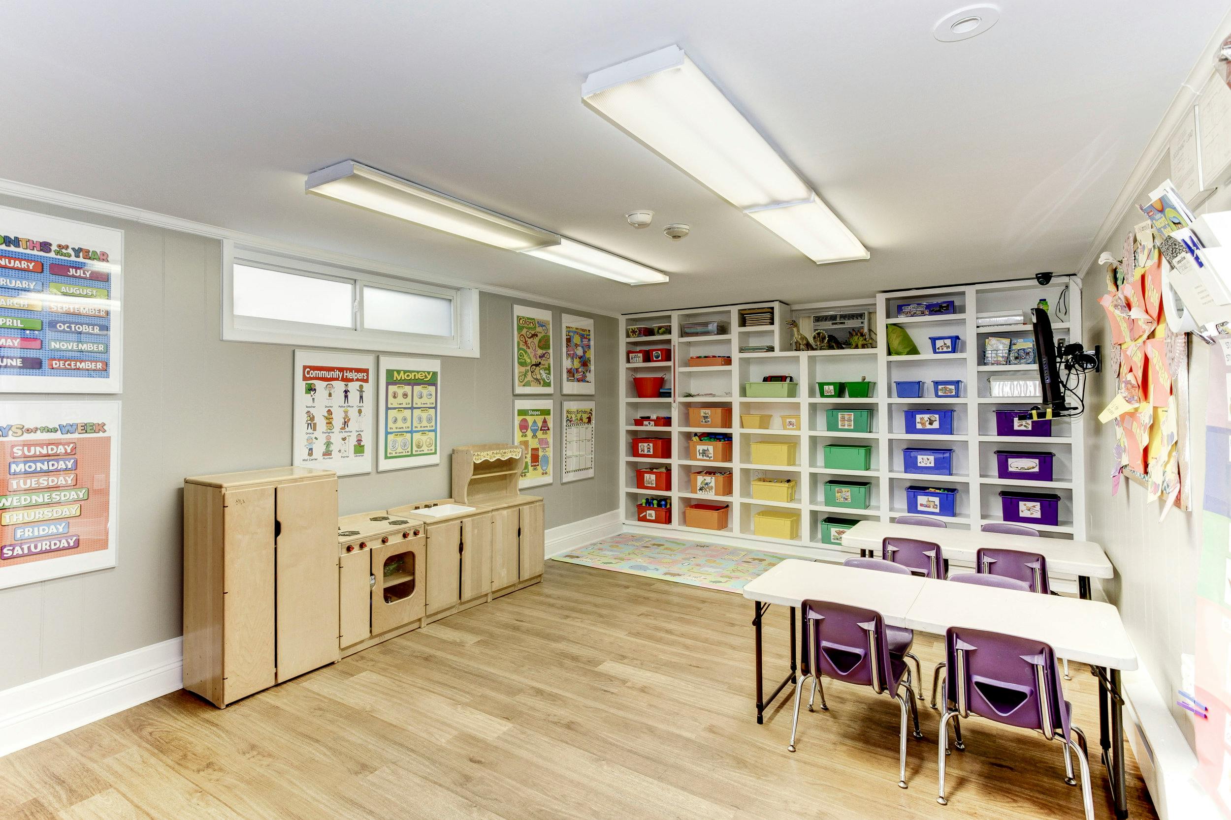 Classroom with tables, chairs, storage shelves, and play kitchen