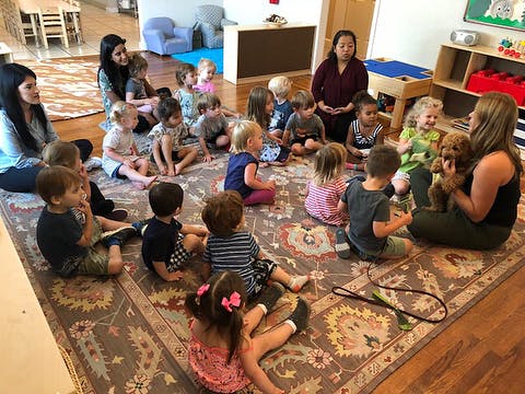 Adults and children sitting on a rug in a classroom