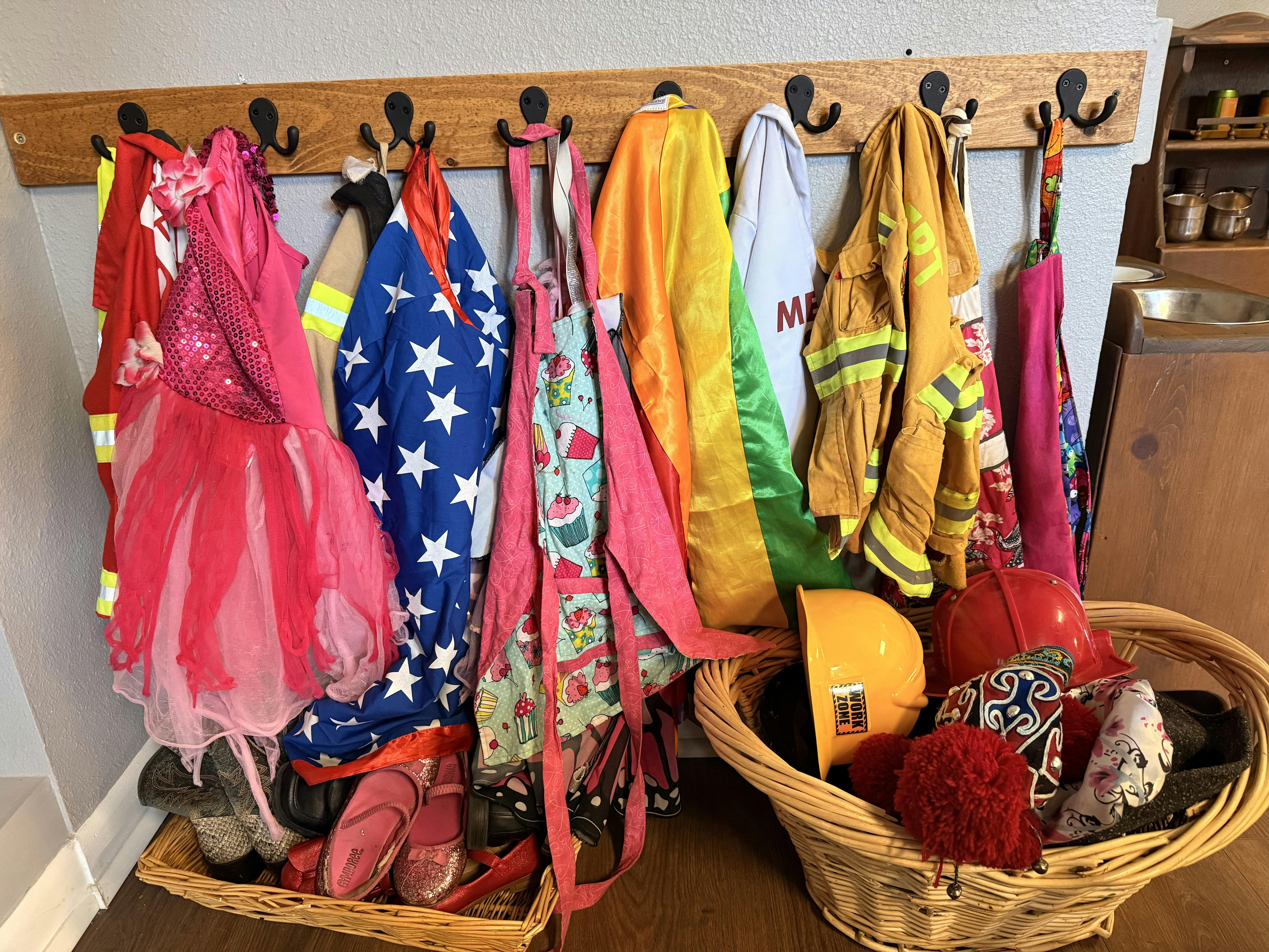 A wooden coat rack with various dress-up clothes, including a firefighter's uniform and princess dresses