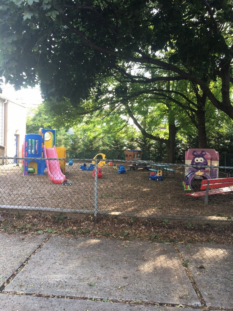 Playground with colorful play structures and a red bench behind a chain-link fence