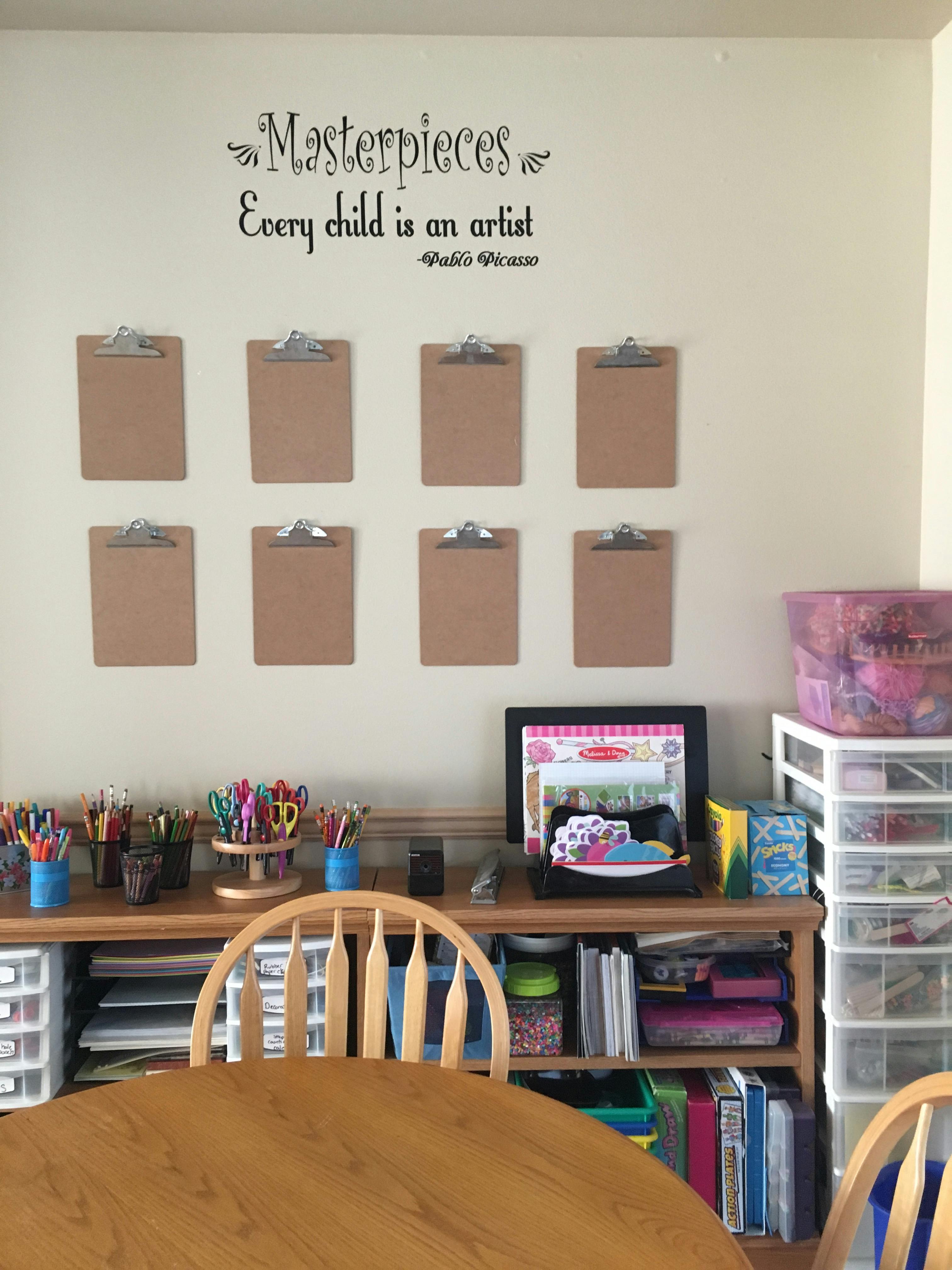 Wall with clipboards, a shelf full of art supplies, and a wooden table