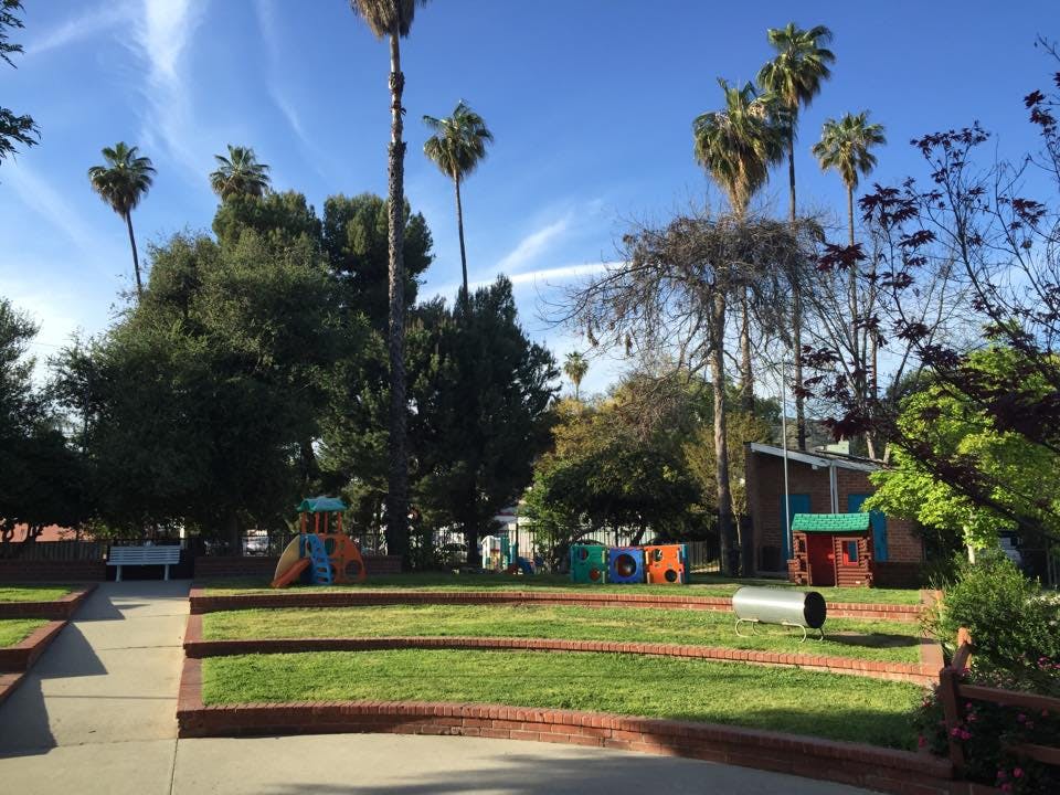 Outdoor playground with grass, trees, and play structures