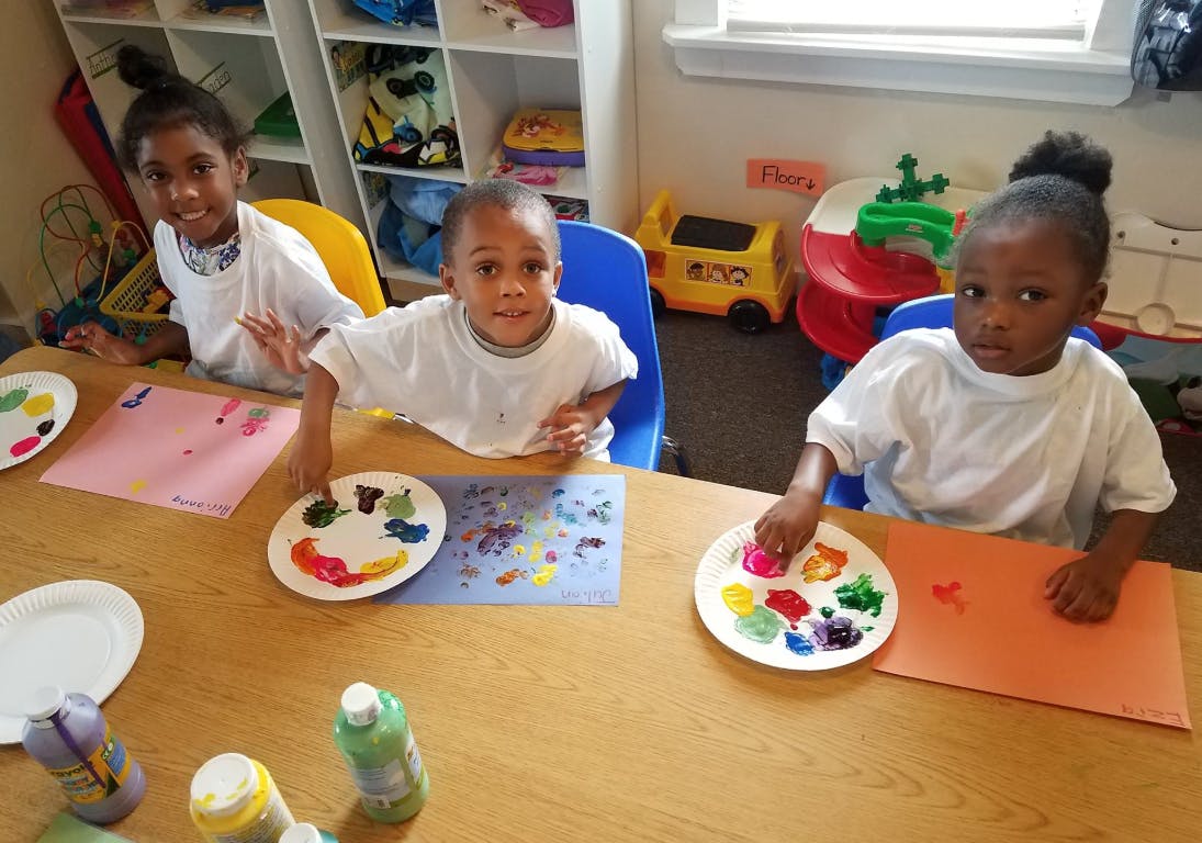 Three children painting at a table in a classroom