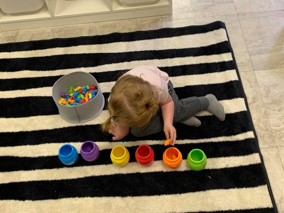Child playing with colorful sorting cups and small objects on a striped rug