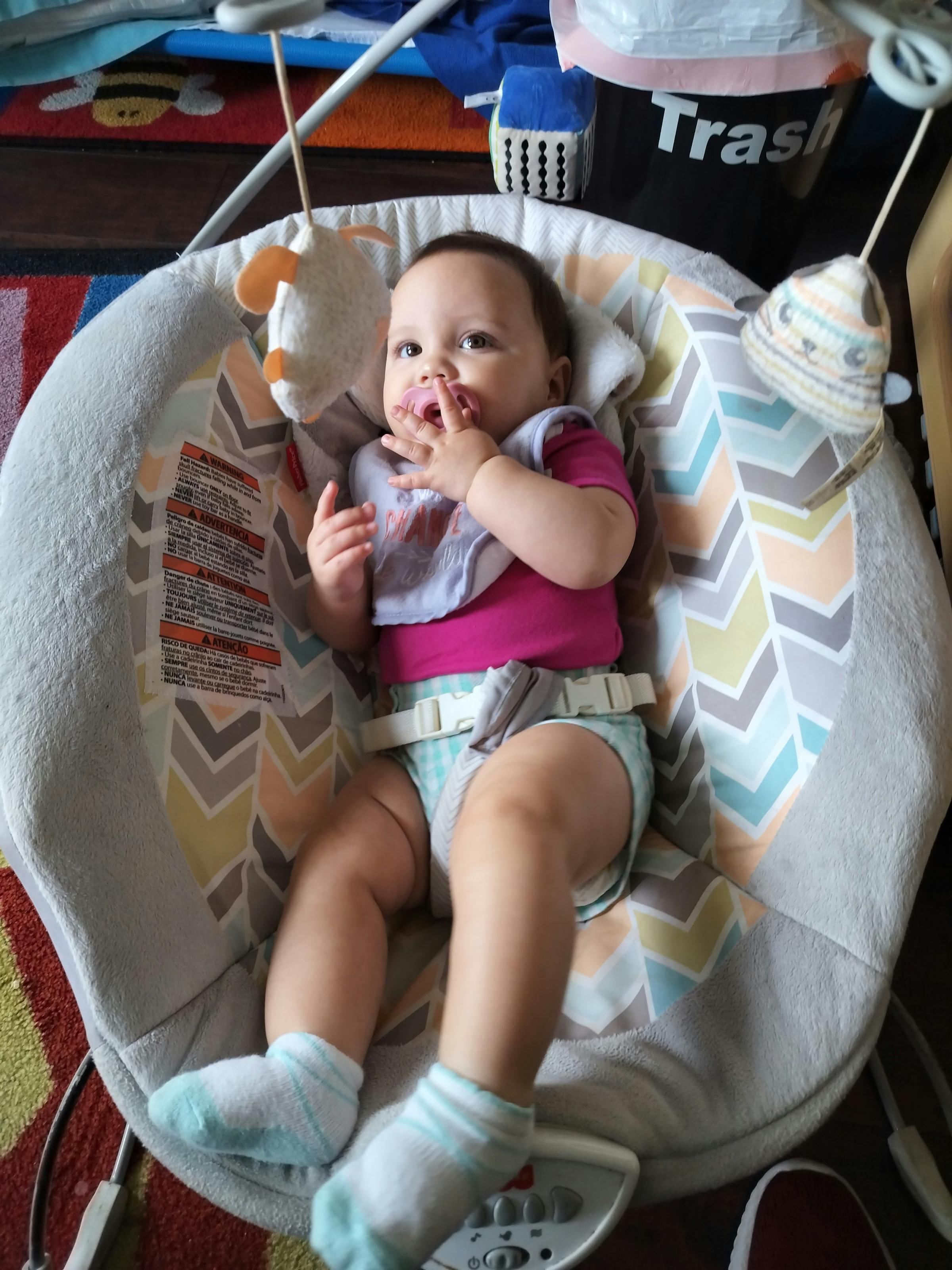 Child in a baby bouncer with hands near mouth