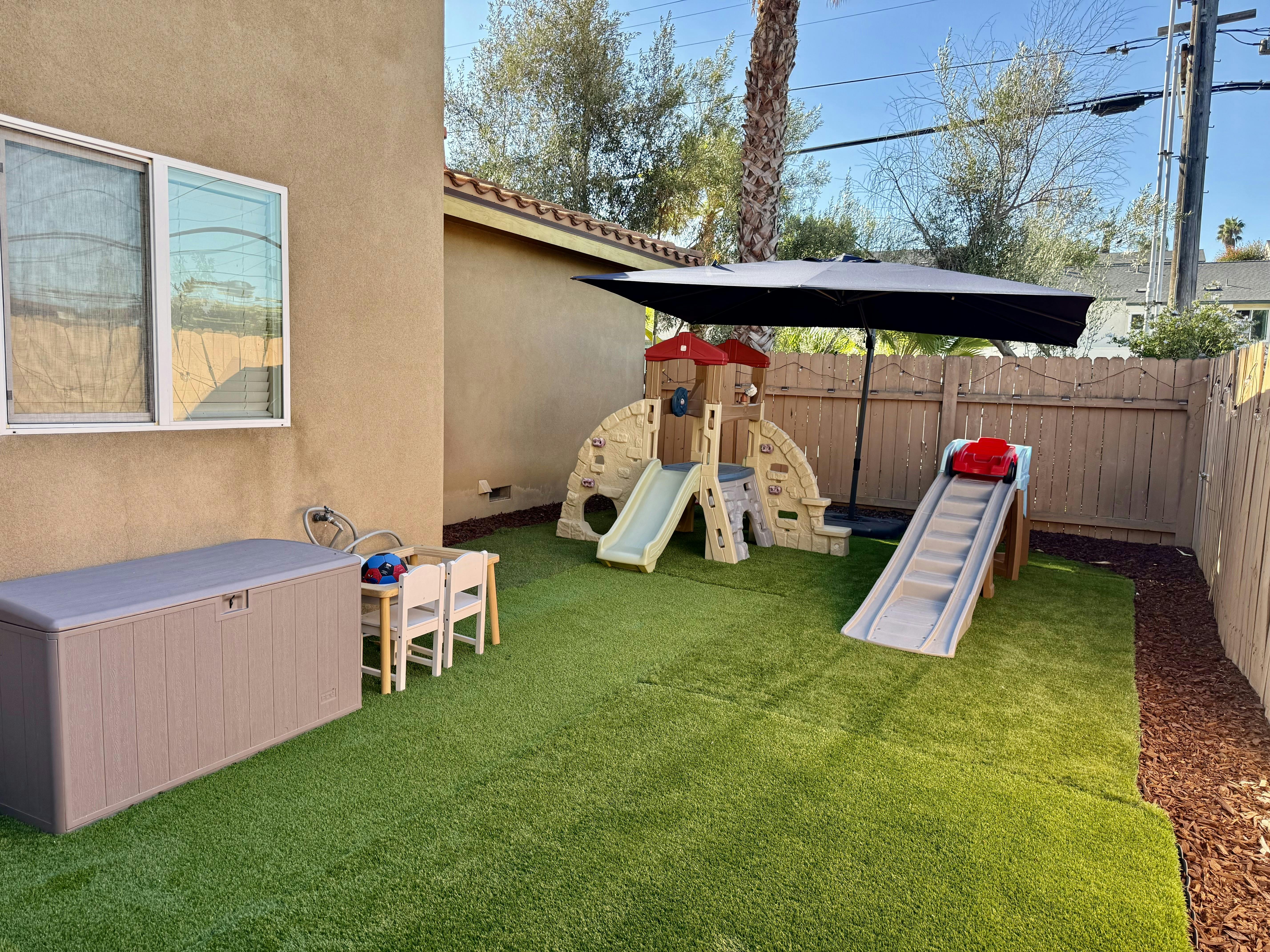 Backyard play area with slides and a table on artificial turf
