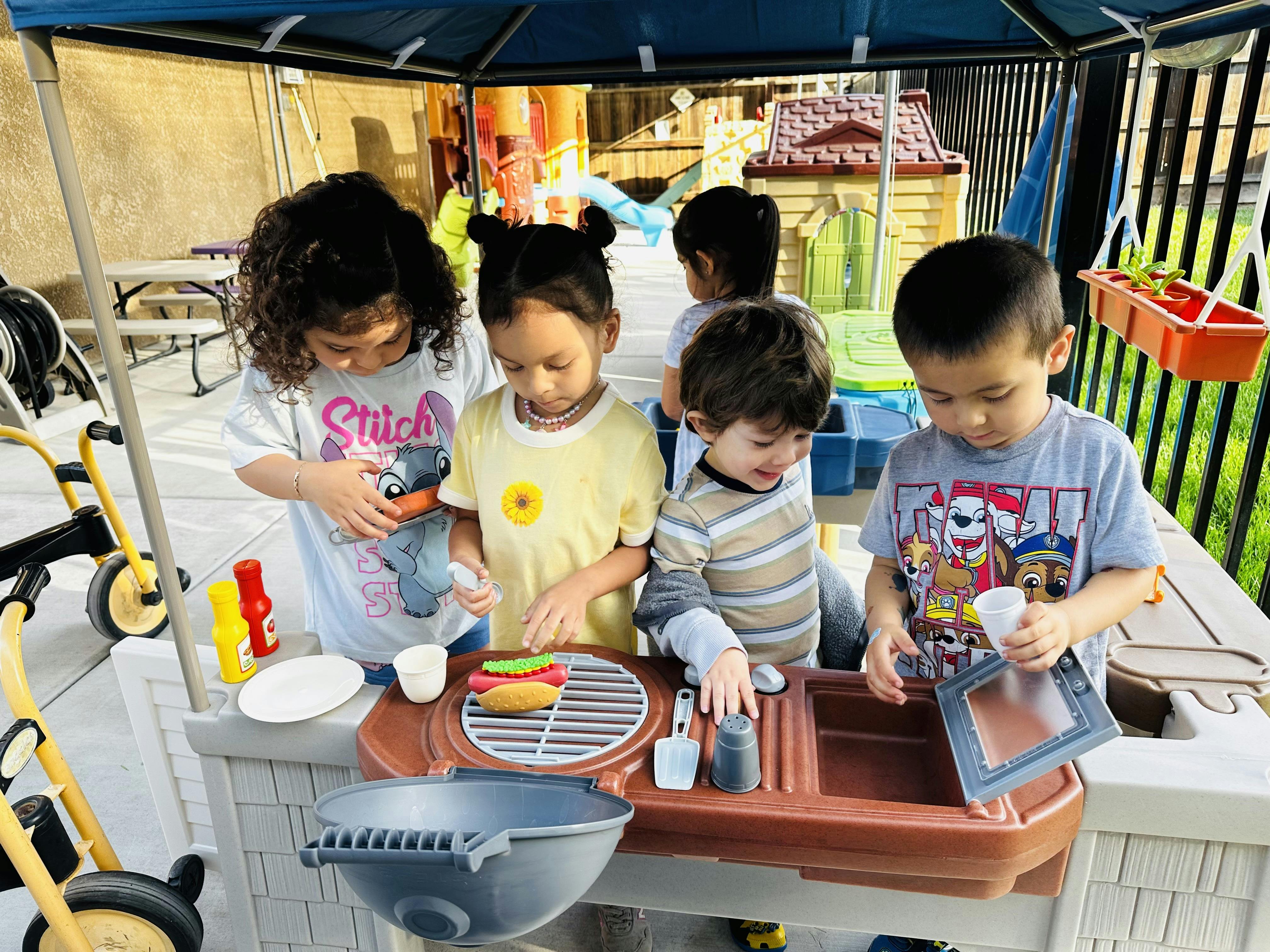 Children gathered around a play kitchen grill set