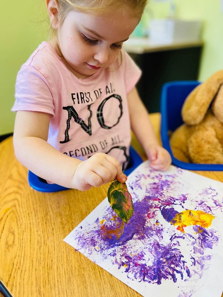 Child making art with a leaf and paint on paper