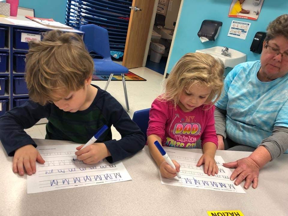 Two children writing on worksheets with a person observing in a classroom