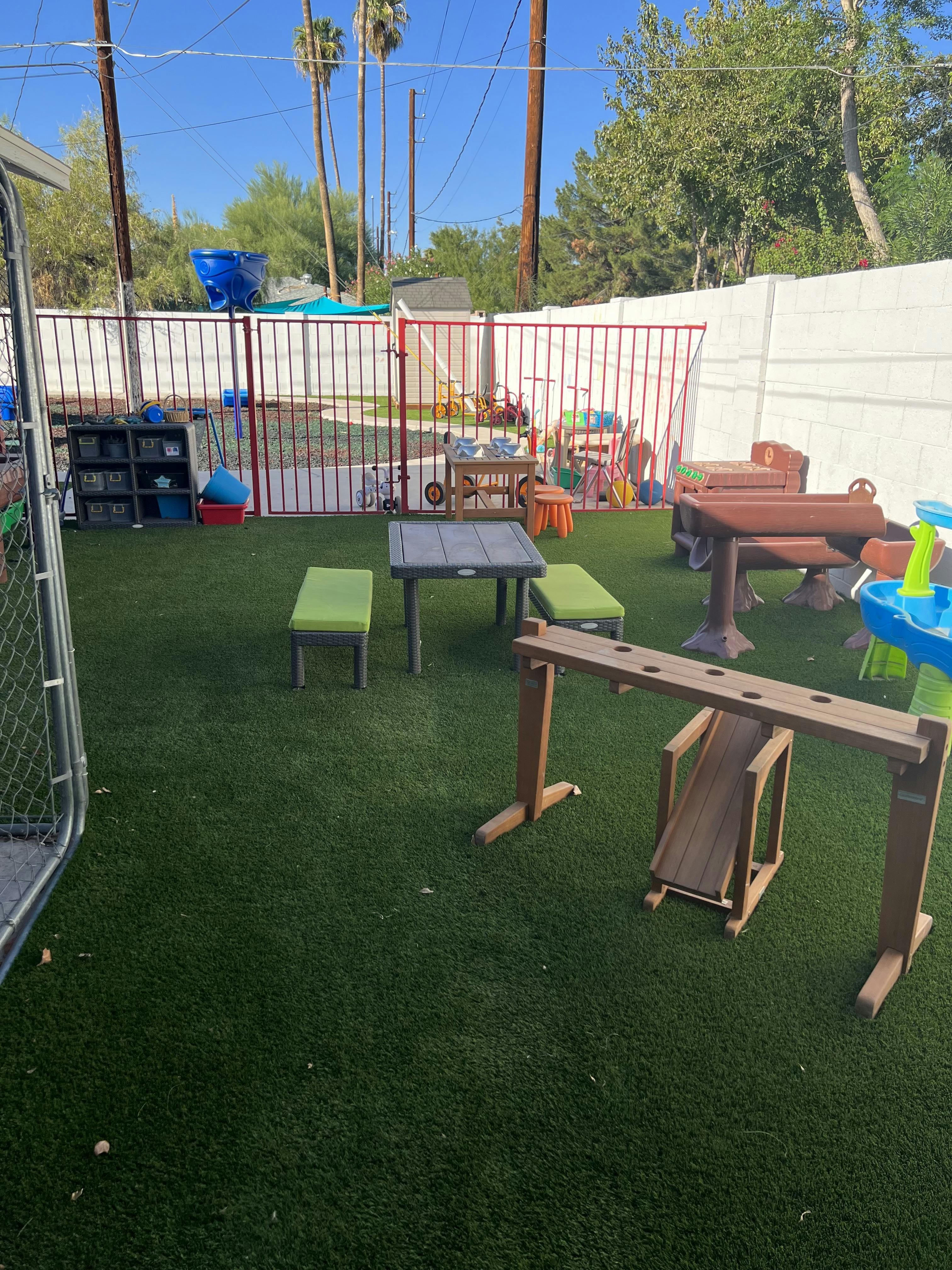 Outdoor play area with artificial turf, tables, benches, and play equipment