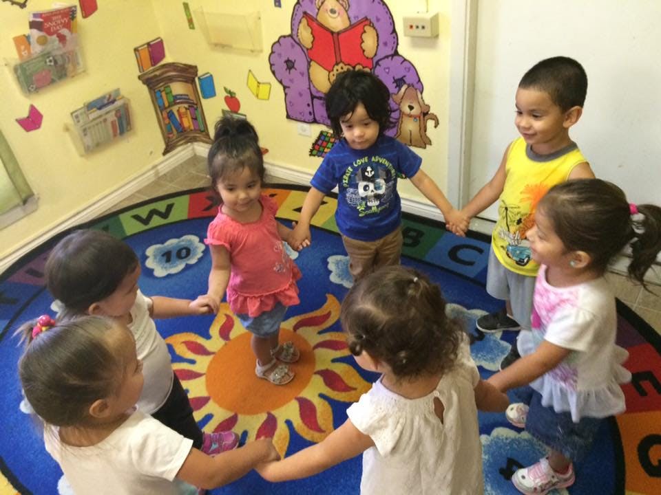 Children holding hands in a circle on a sun-patterned rug