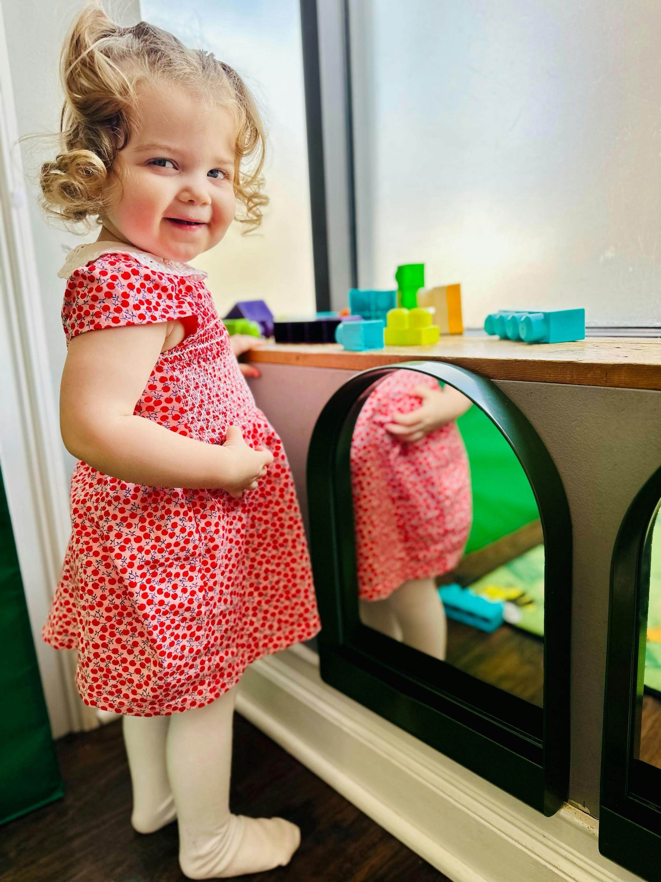 Child in a red dress standing next to a mirror