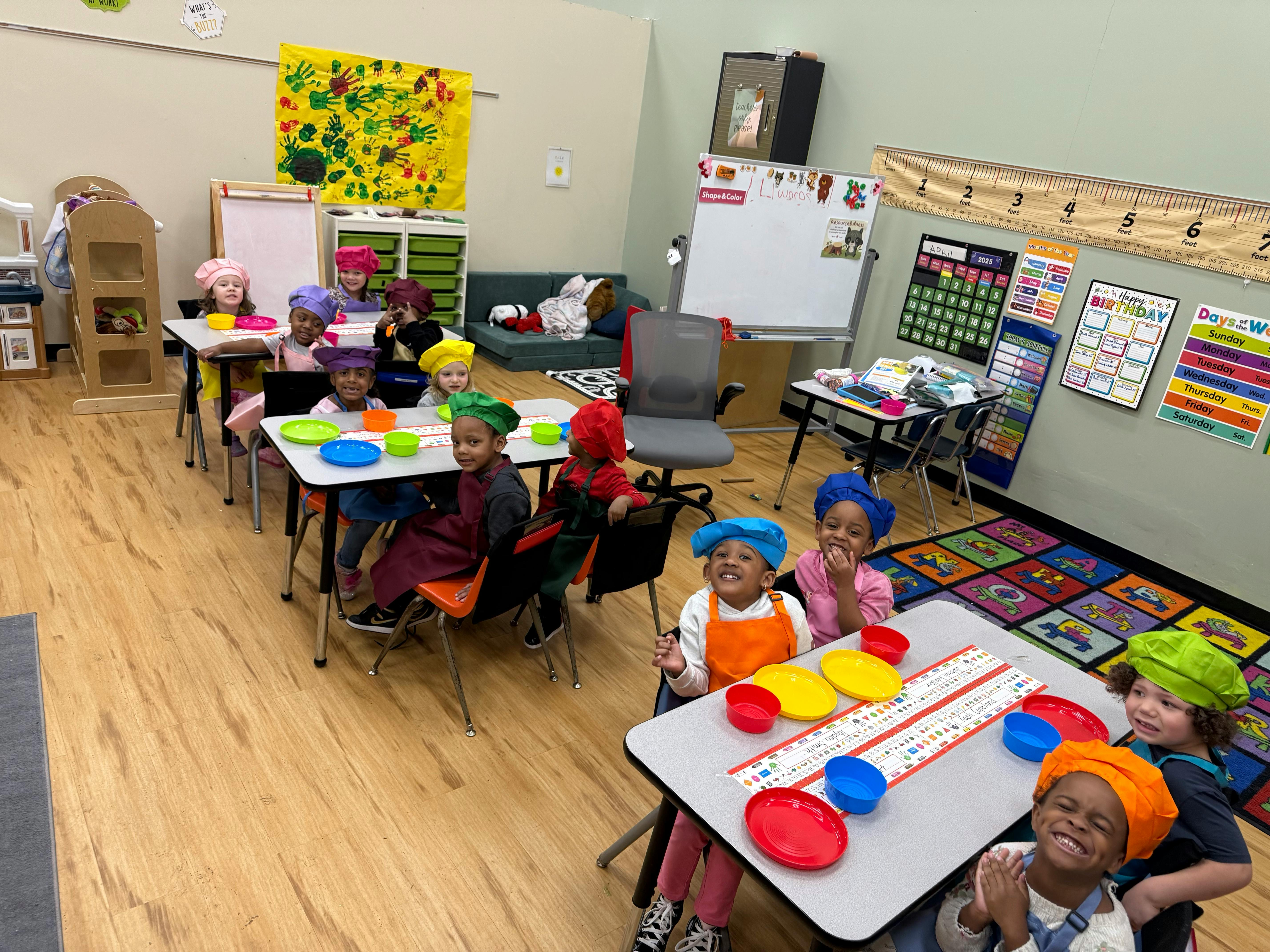 Children in chef hats and aprons sitting at tables in a classroom